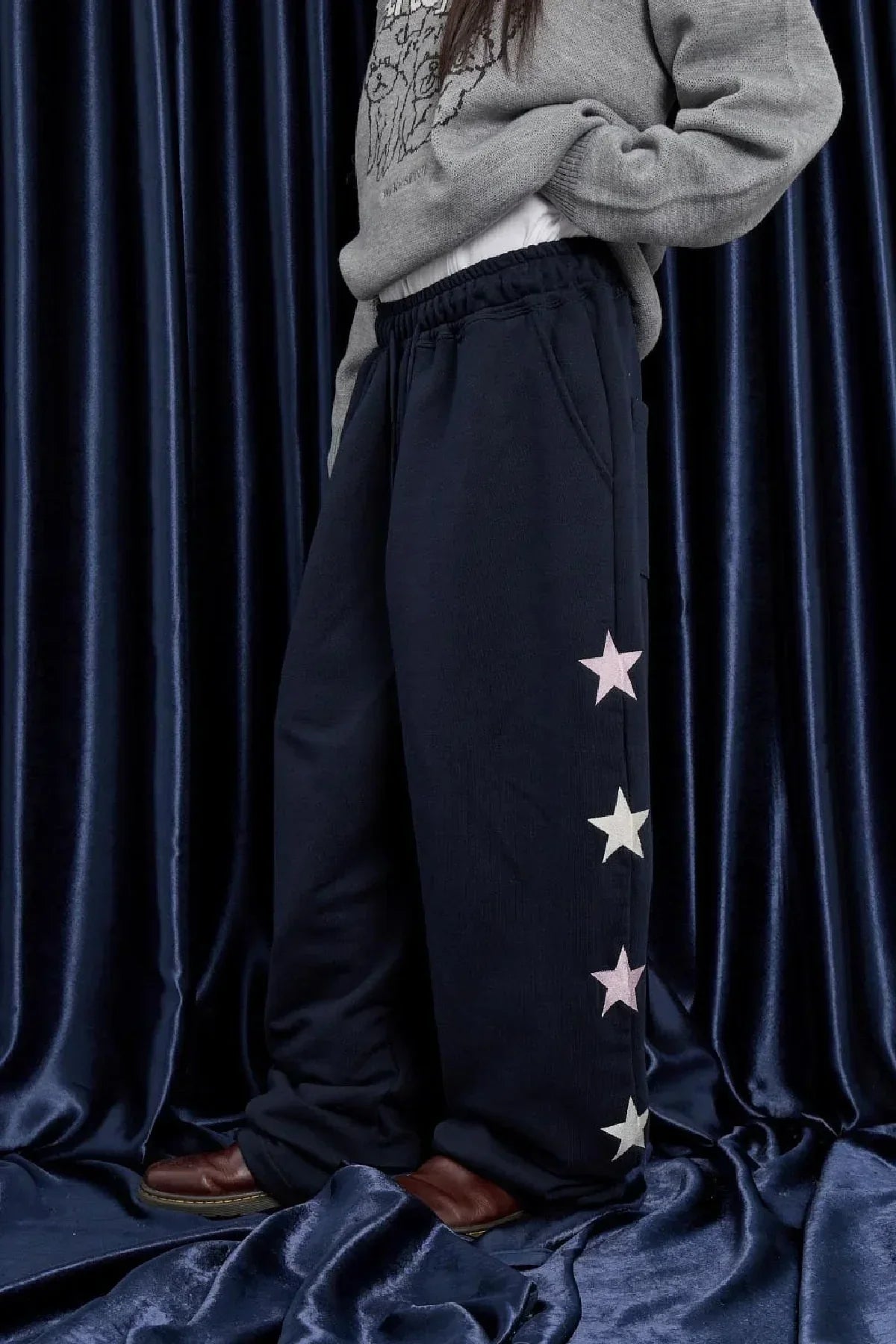 Person wearing navy sweatpants with pink and white star prints on side, standing on dark blue velvet fabric