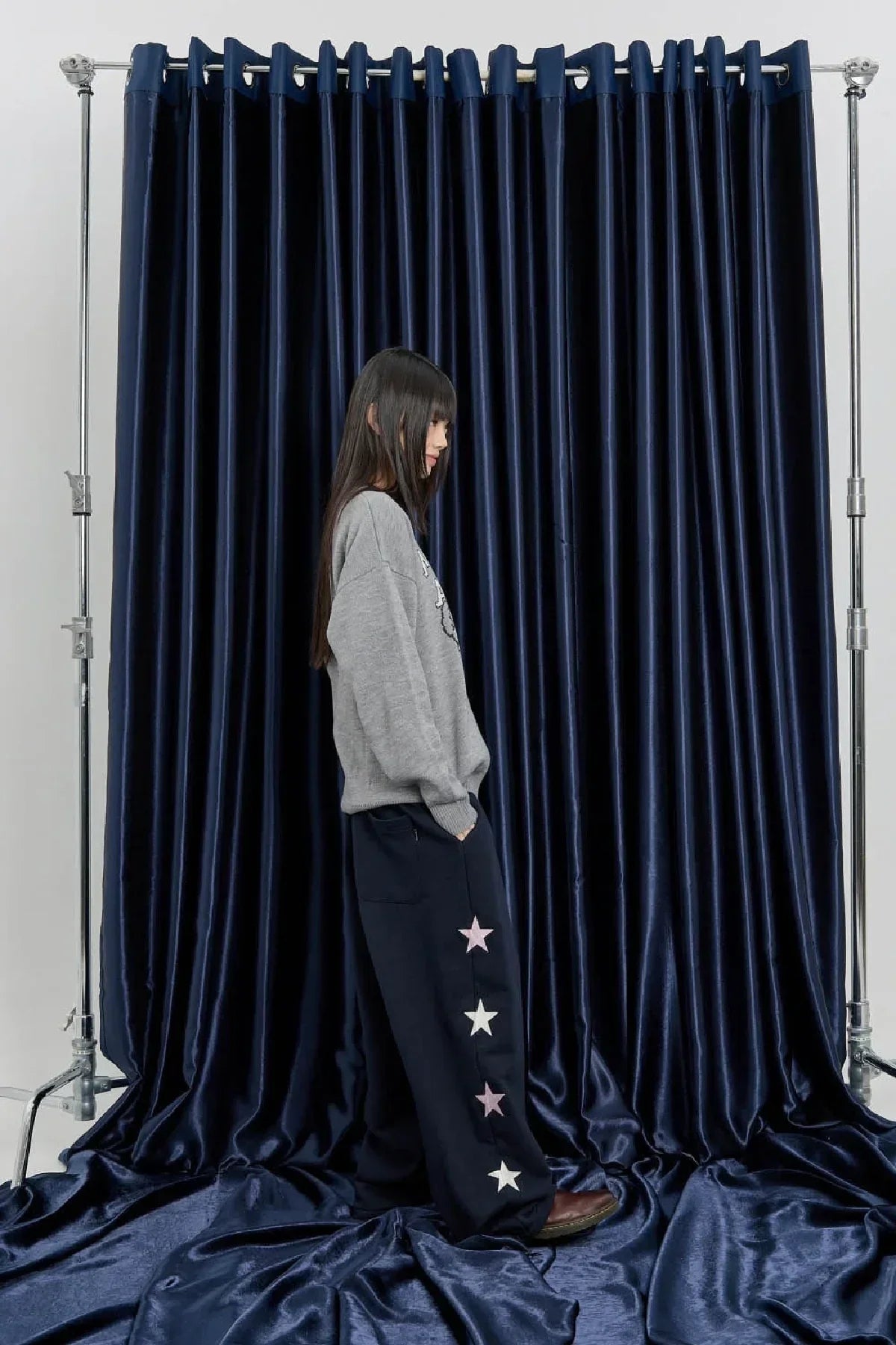 Woman wearing navy star sweatpants and gray sweater posing against dark blue velvet curtain backdrop