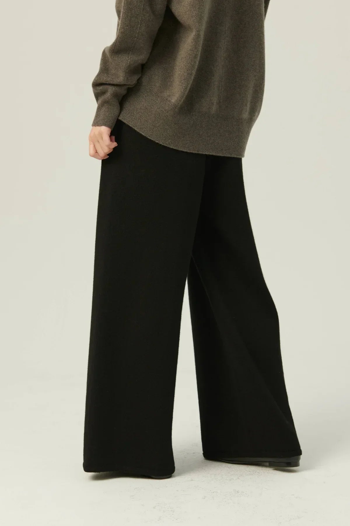 Model wearing black straight-fit knit pants and olive green sweater on light background