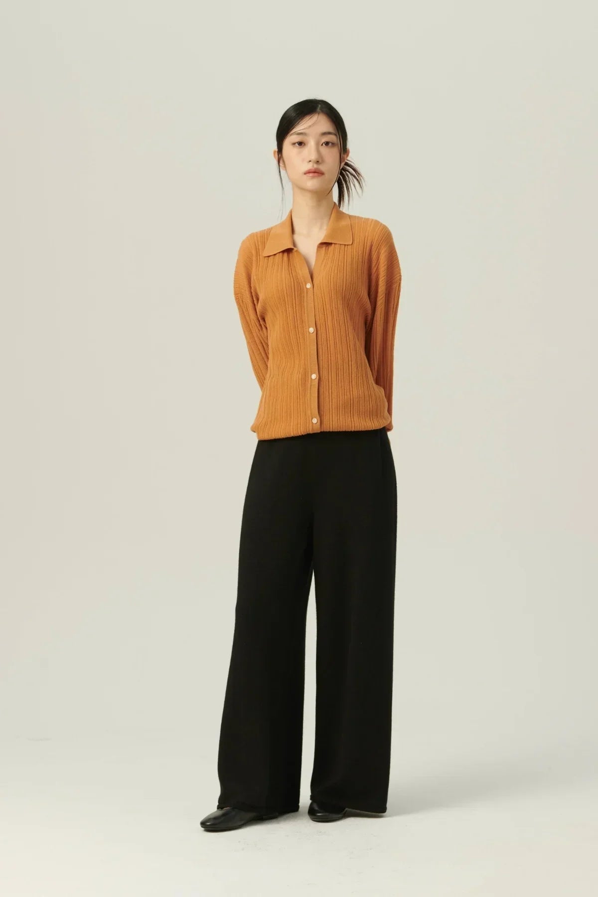 Woman wearing black straight-fit knit pants and a brown ribbed button-up cardigan