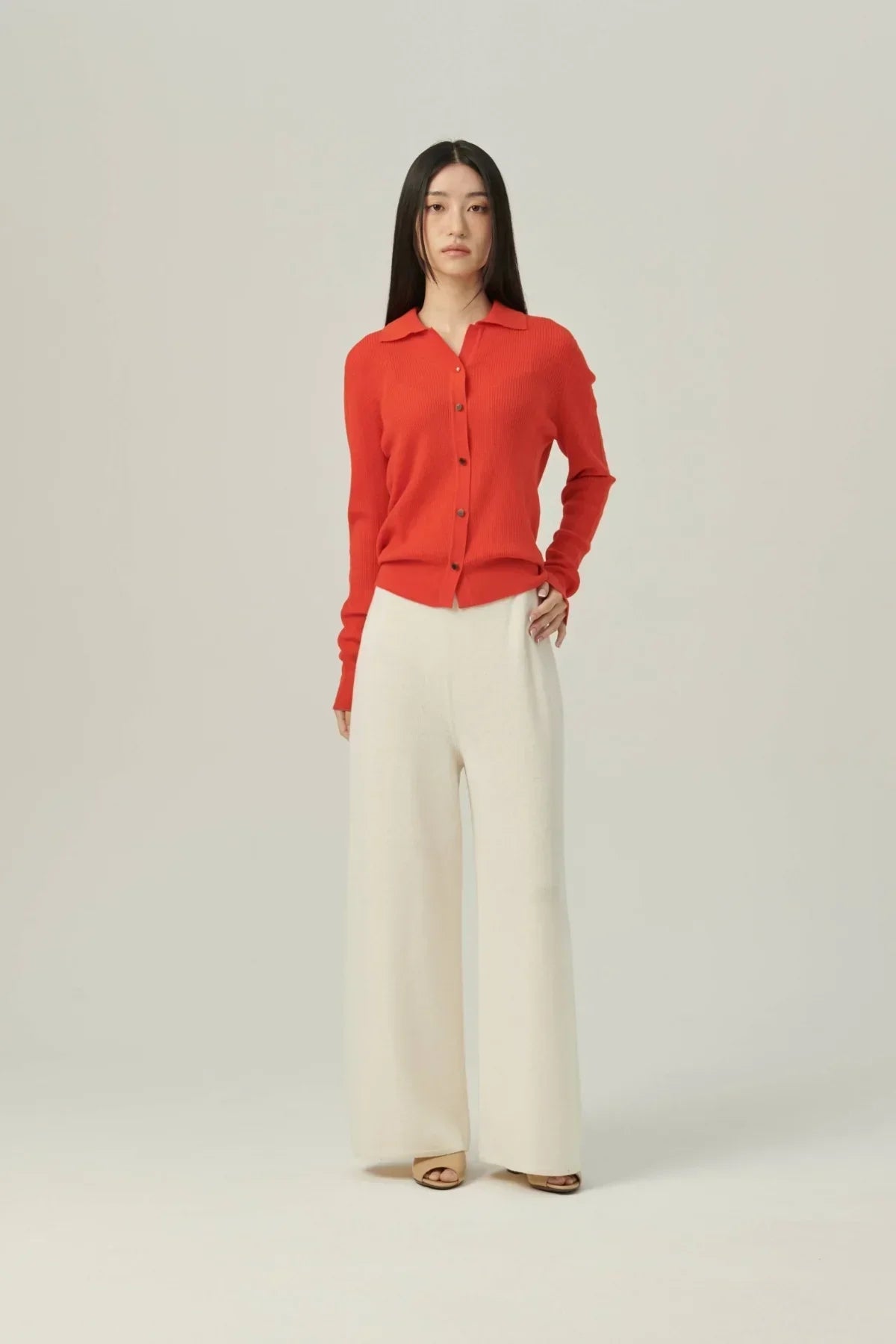 Model wearing white wide-leg knit pants and a red button-up cardigan against a plain background
