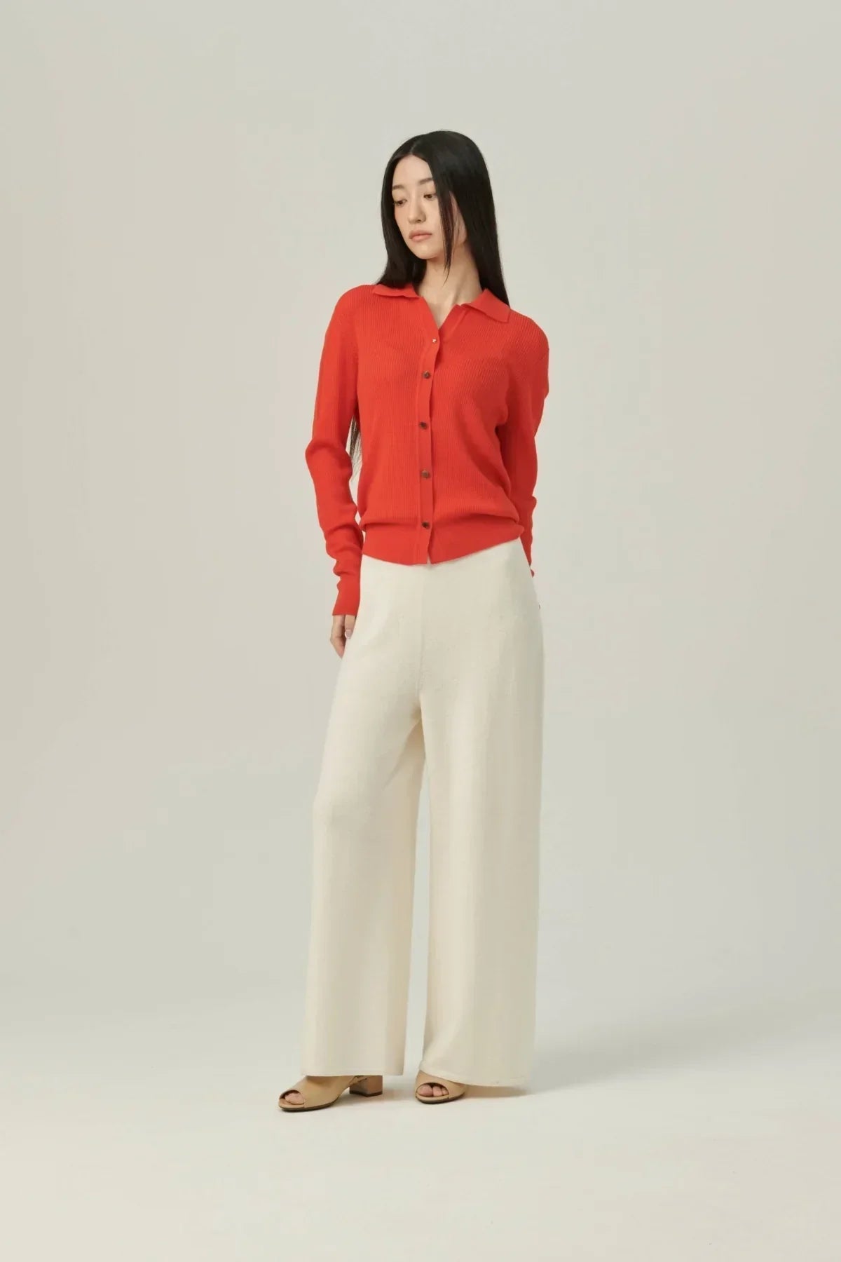 Woman wearing red button-up sweater and white wide-leg knit pants with beige open-toe heels
