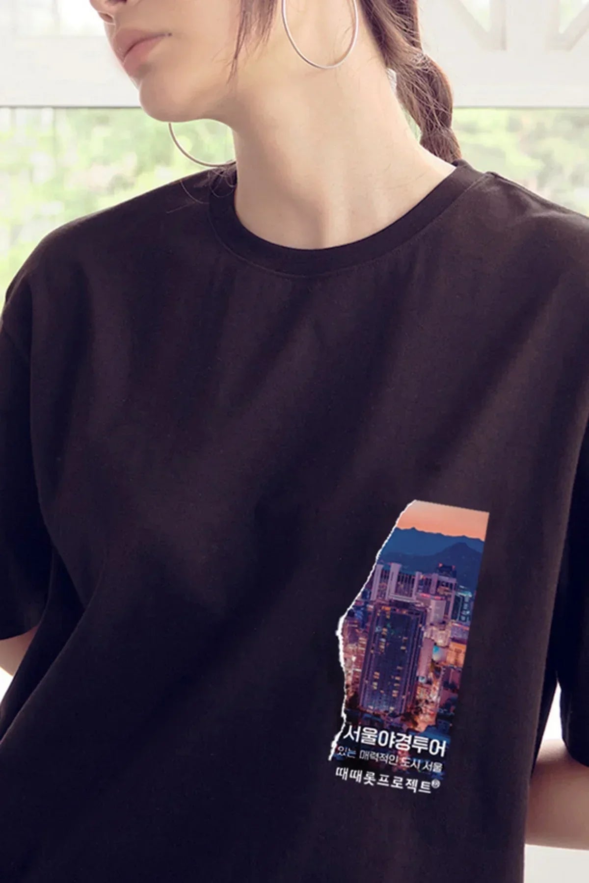 Woman wearing black t-shirt with colorful Seoul cityscape graphic and Korean text on chest