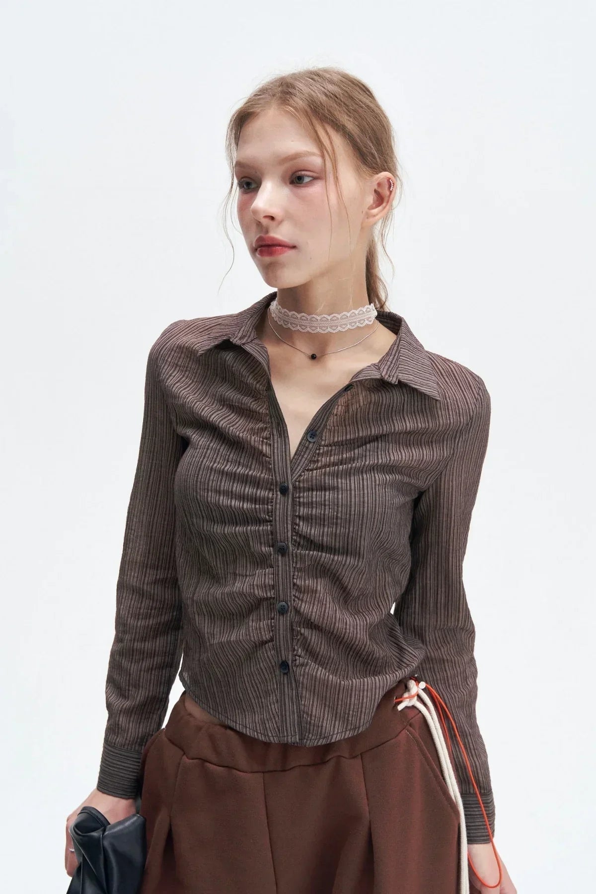 Young woman wearing brown striped cropped button-up shirt and brown pants with white rope detail