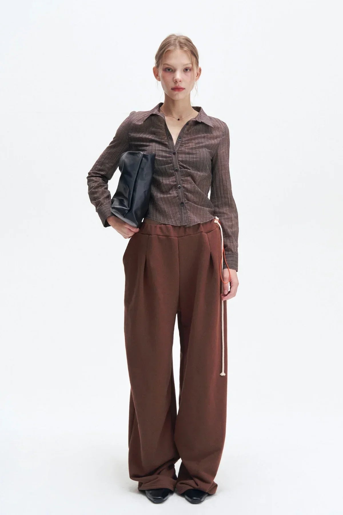 Model wearing brown striped cropped shirt with wide-leg brown pants and holding a black clutch