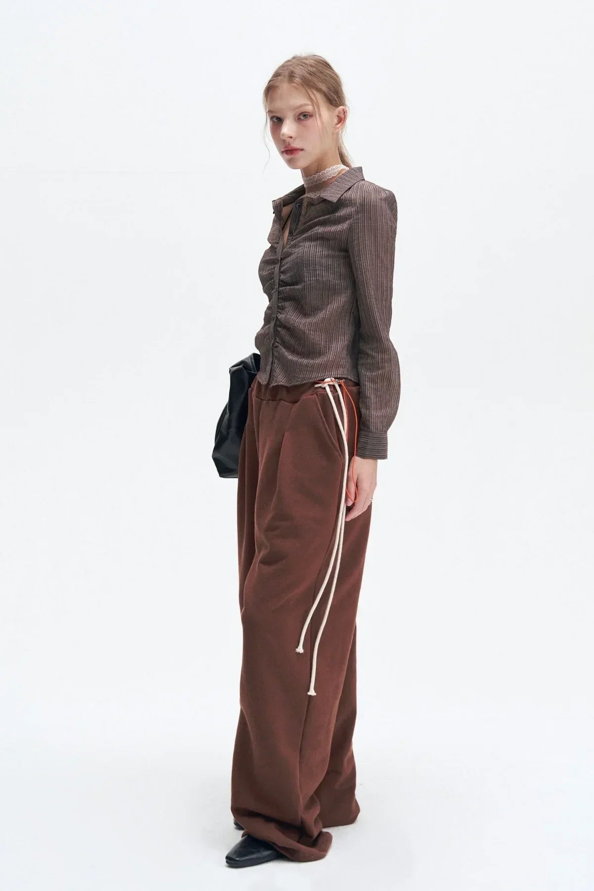 Model wearing brown striped ruched shirt, wide brown pants with white drawstrings, black bag, and black shoes