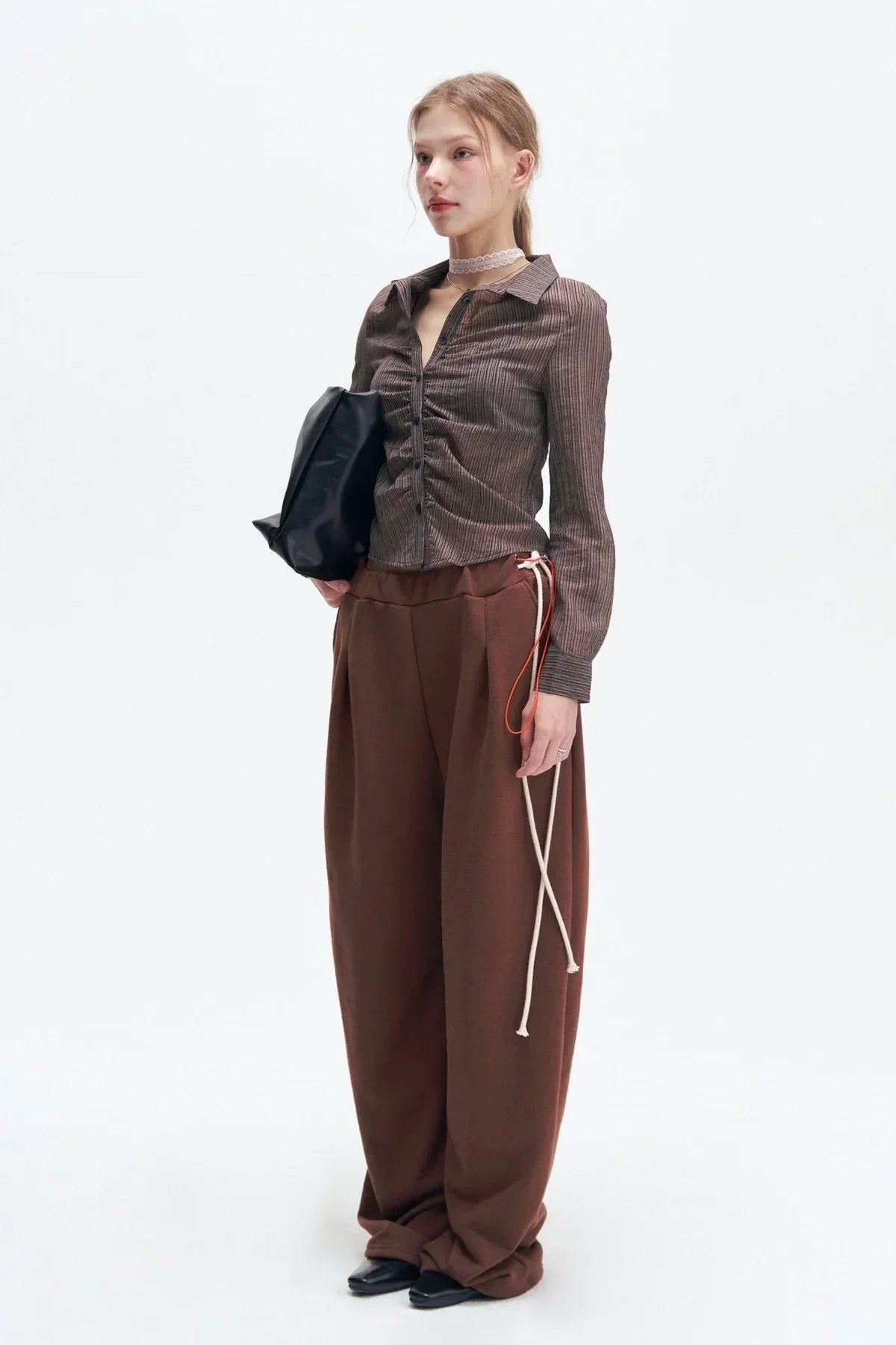 Woman wearing brown striped ruched shirt, wide brown pants, black shoes, holding black bag