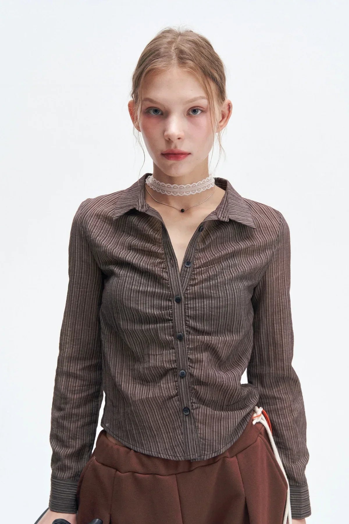 Young woman wearing a fitted brown striped button-up shirt and brown pants in studio