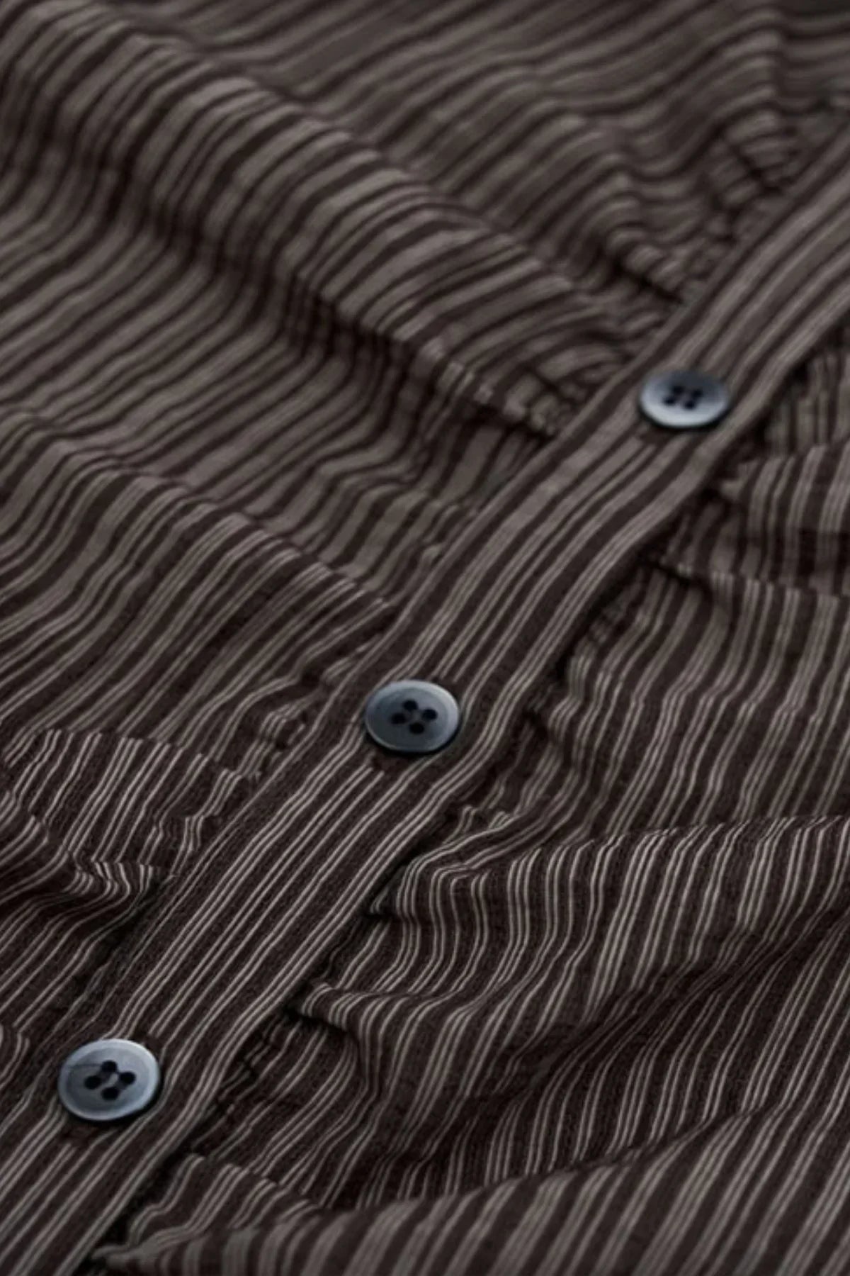 close-up of brown striped fabric with vertical lines and dark buttons on a shirt