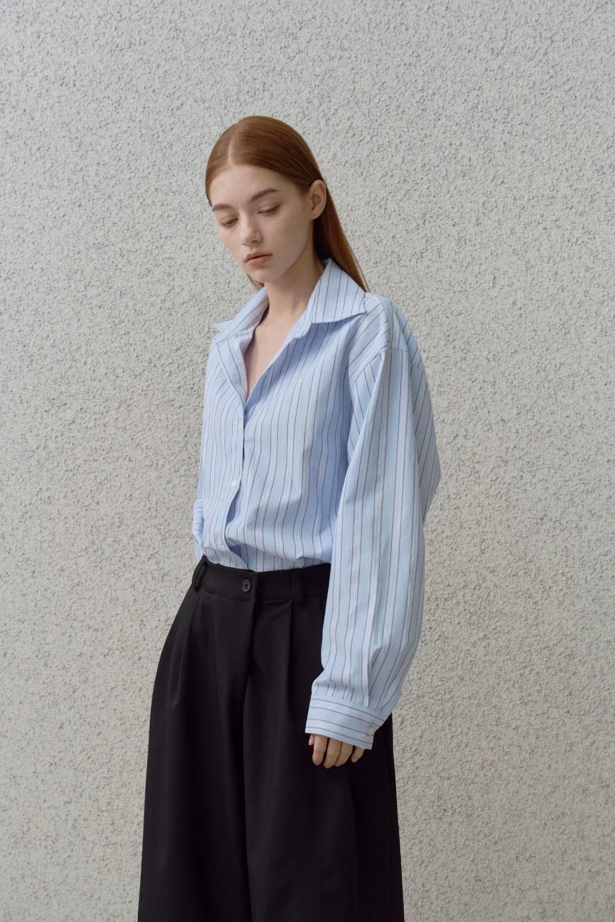 Model wearing light blue vertical striped oversized shirt and black high-waisted wide-leg trousers