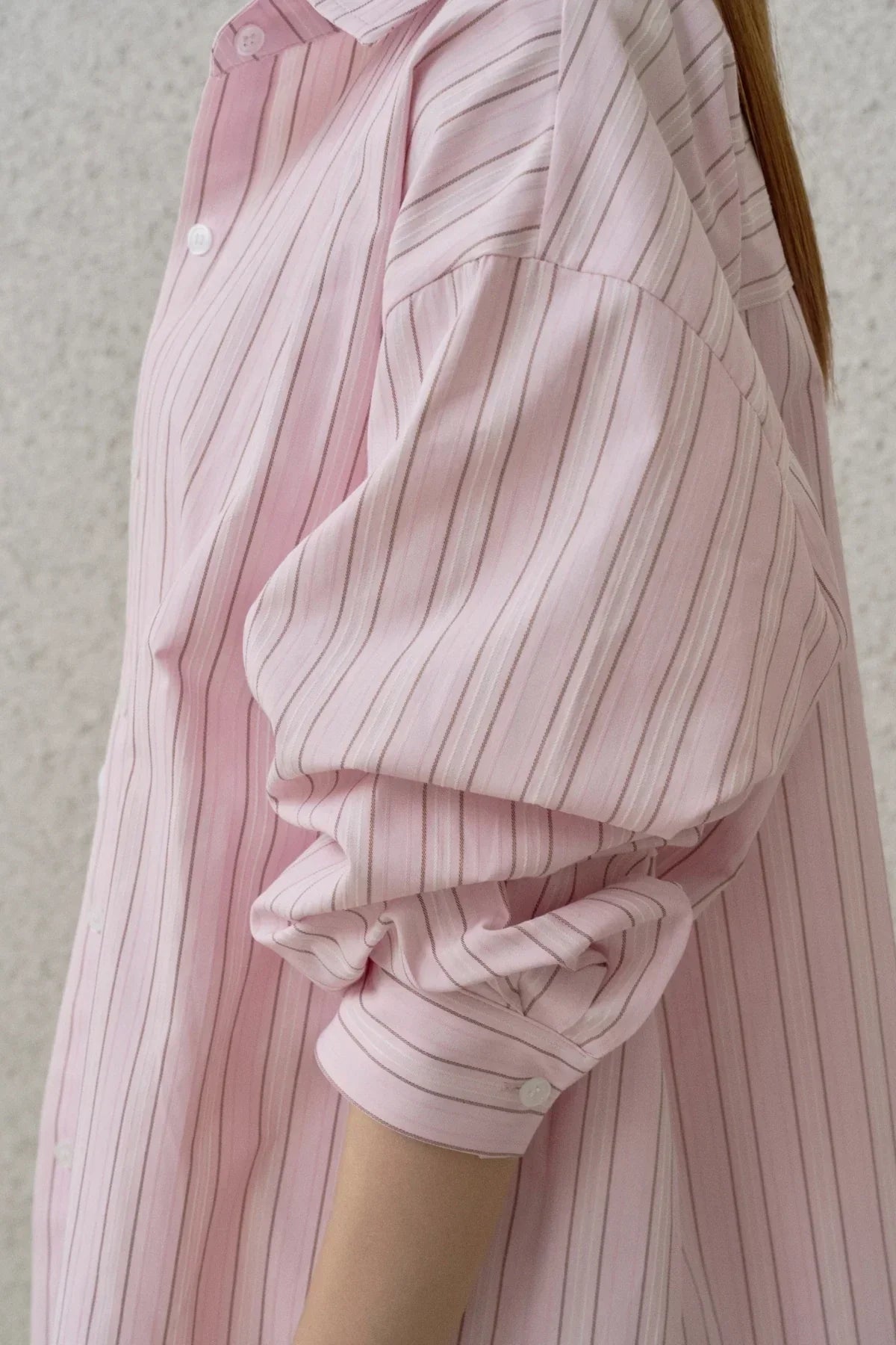 Close-up of a pink striped button-up shirt with rolled-up sleeves, lightweight fabric