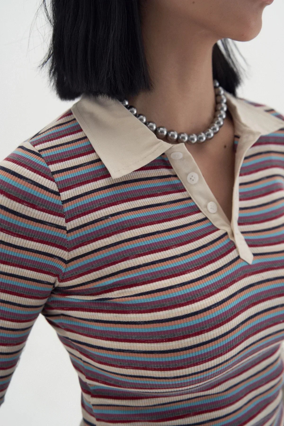 Close-up of a woman wearing a striped multicolor polo shirt with a beige collar and silver bead necklace