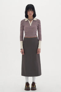 Woman wearing striped long-sleeve polo shirt, brown midi skirt, white socks, and sneakers on white background