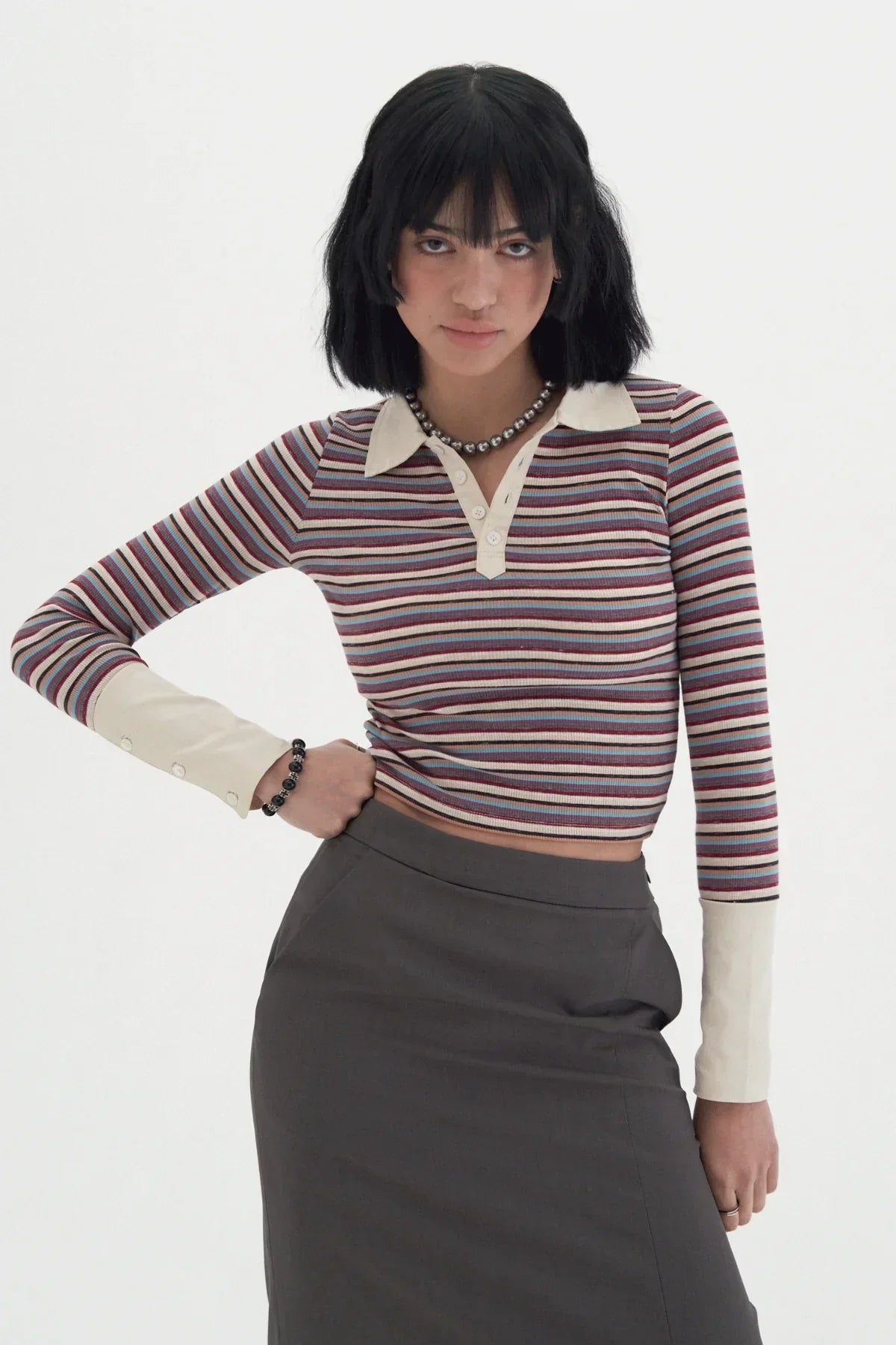 Young woman wearing a striped long-sleeve polo shirt with beige collar and cuffs, paired with a dark skirt