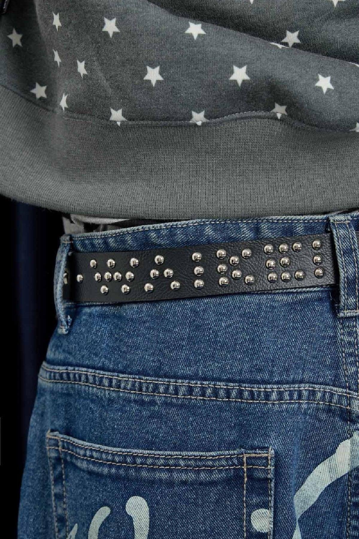 Close-up of black studded belt worn with blue denim jeans and gray star-patterned sweater