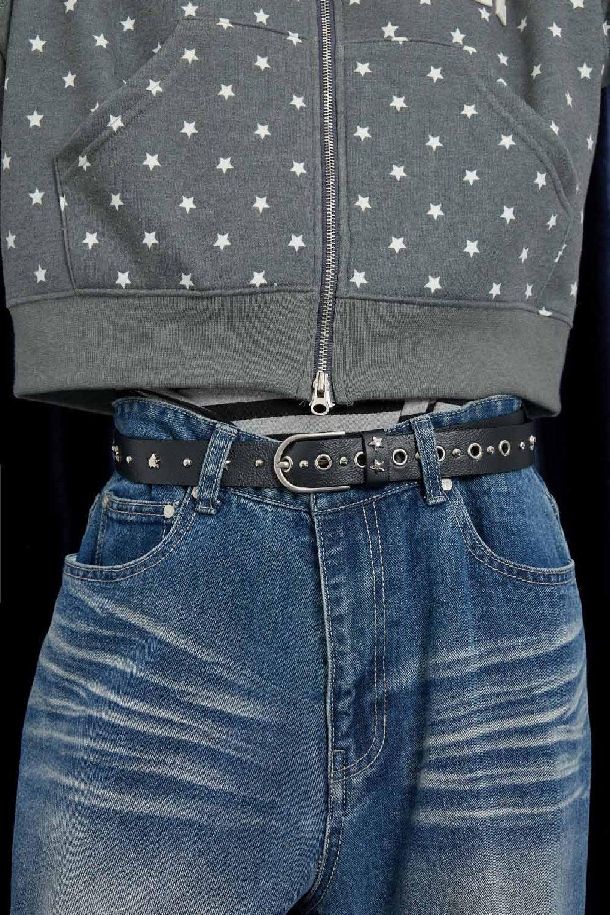 Black leather belt with silver studs and star details worn with blue denim jeans and gray star-patterned hoodie