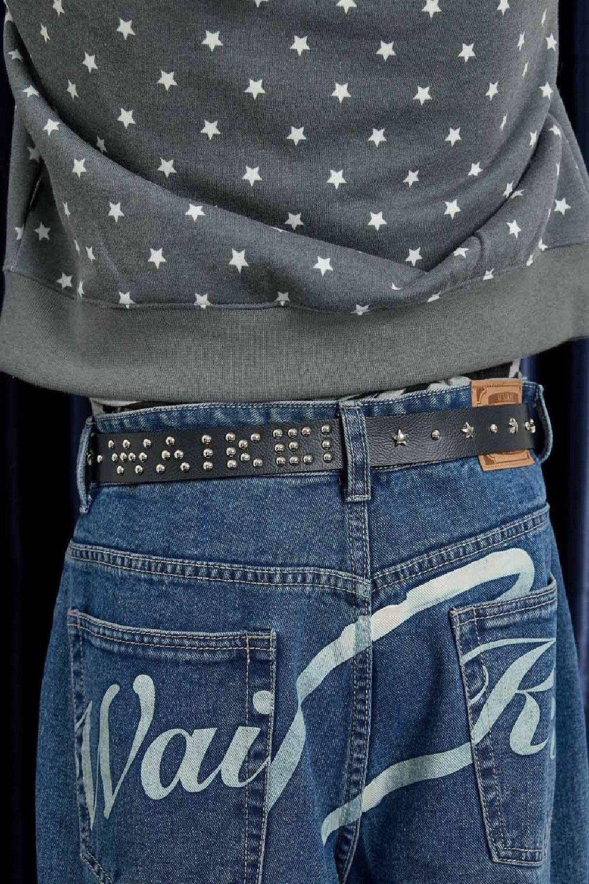 Black leather studded belt with silver round studs and star accents worn with blue denim jeans and star-patterned gray sweatshirt
