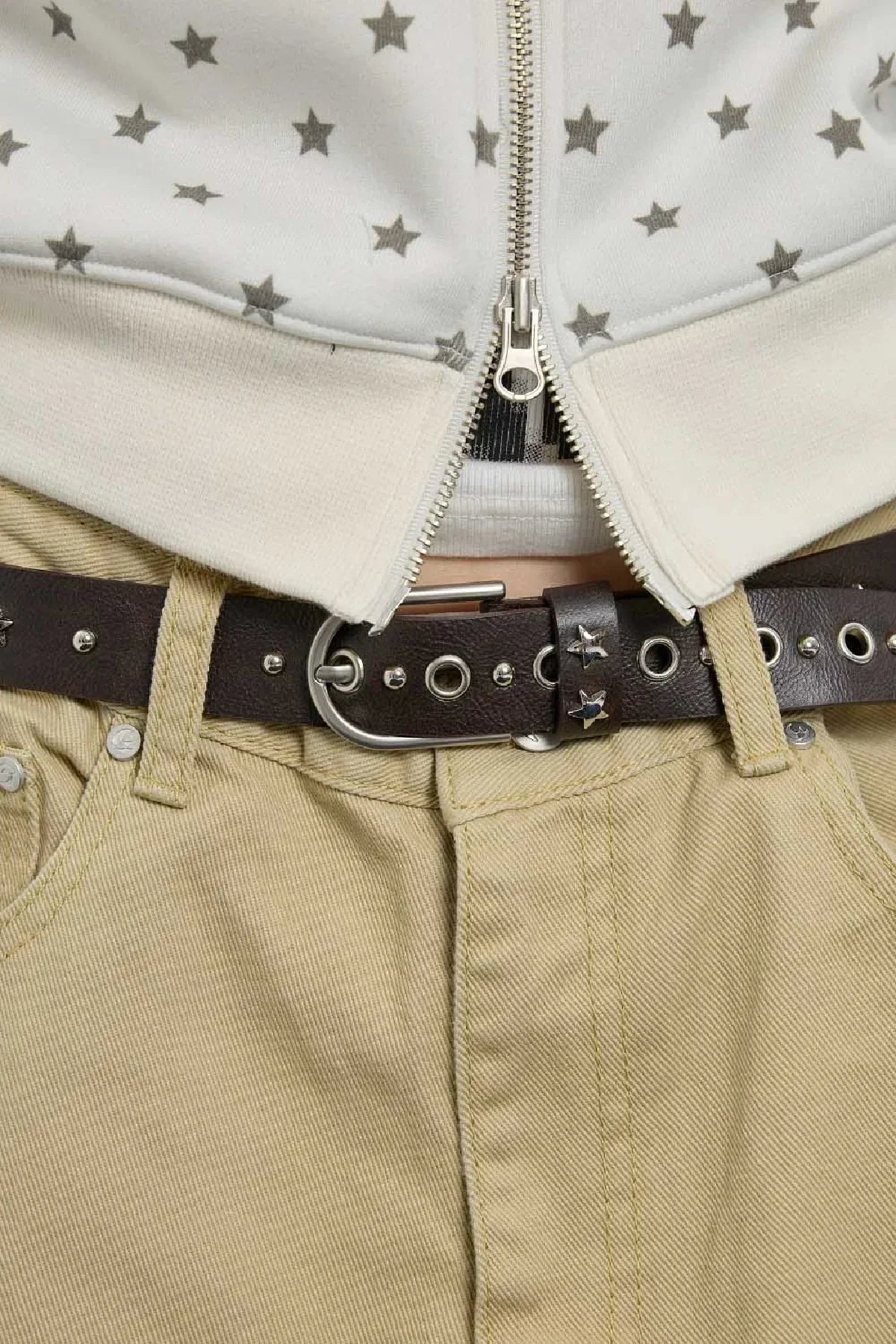 Close-up of brown leather belt with metal studs and star-shaped decorations on beige pants