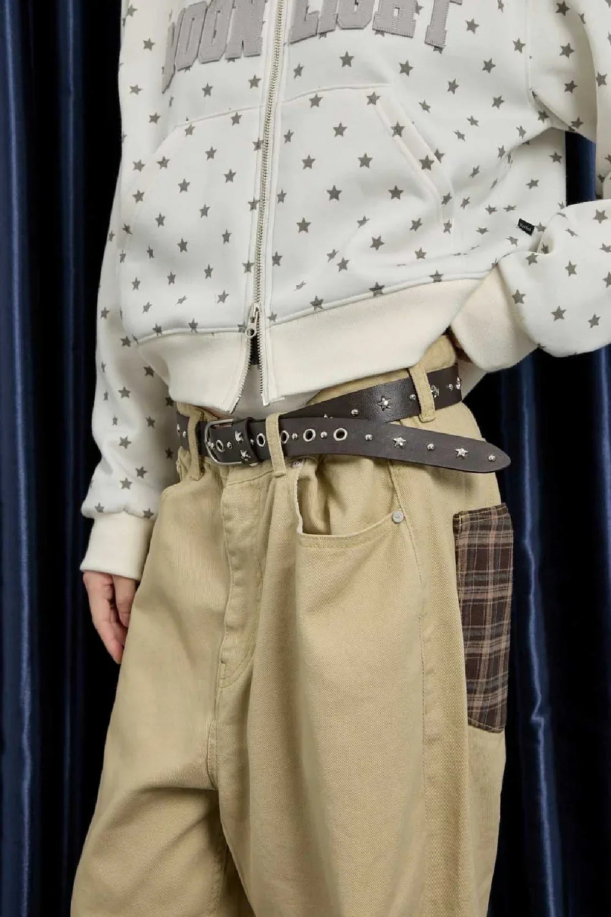 Close-up of person wearing beige pants with plaid side pocket and brown studded leather belt