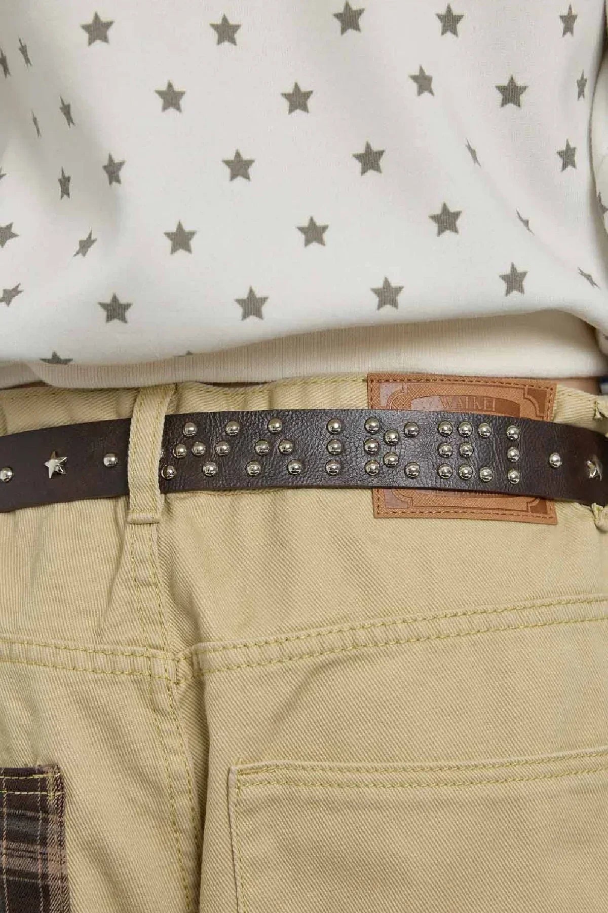 Close-up of a brown studded leather belt with star studs worn with beige pants and a white star-patterned top