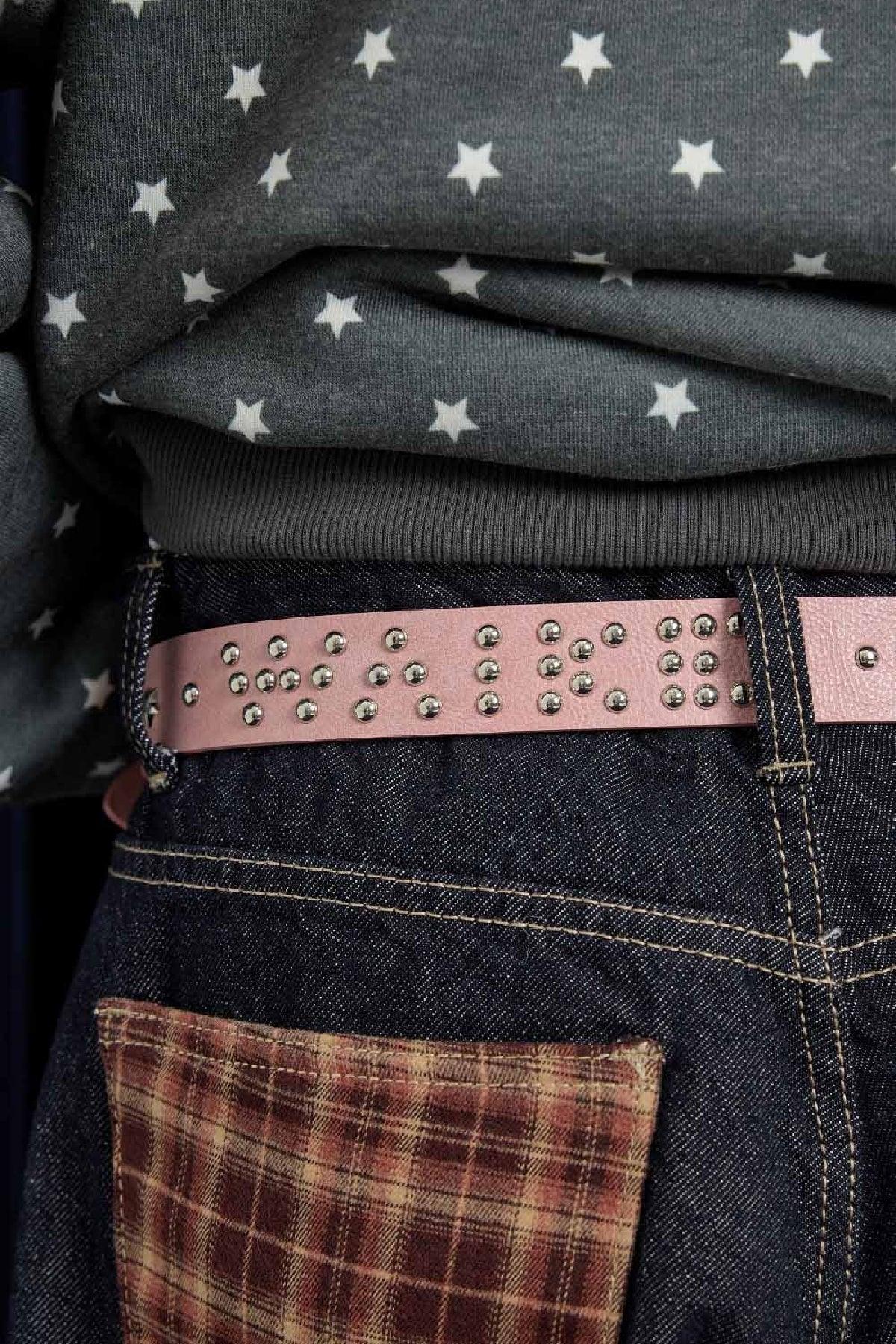 Close-up of pink studded belt with metal studs worn with dark denim jeans and star-patterned sweater