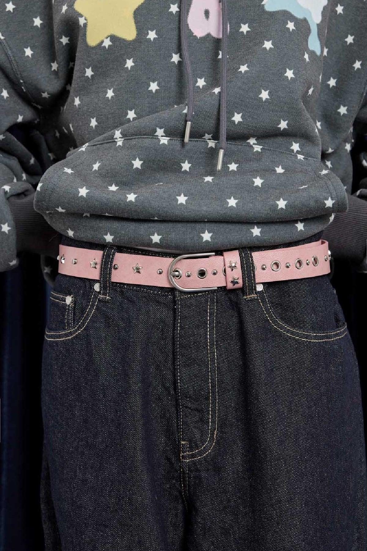 Close-up of pink studded belt with star and round metal accents on dark denim jeans