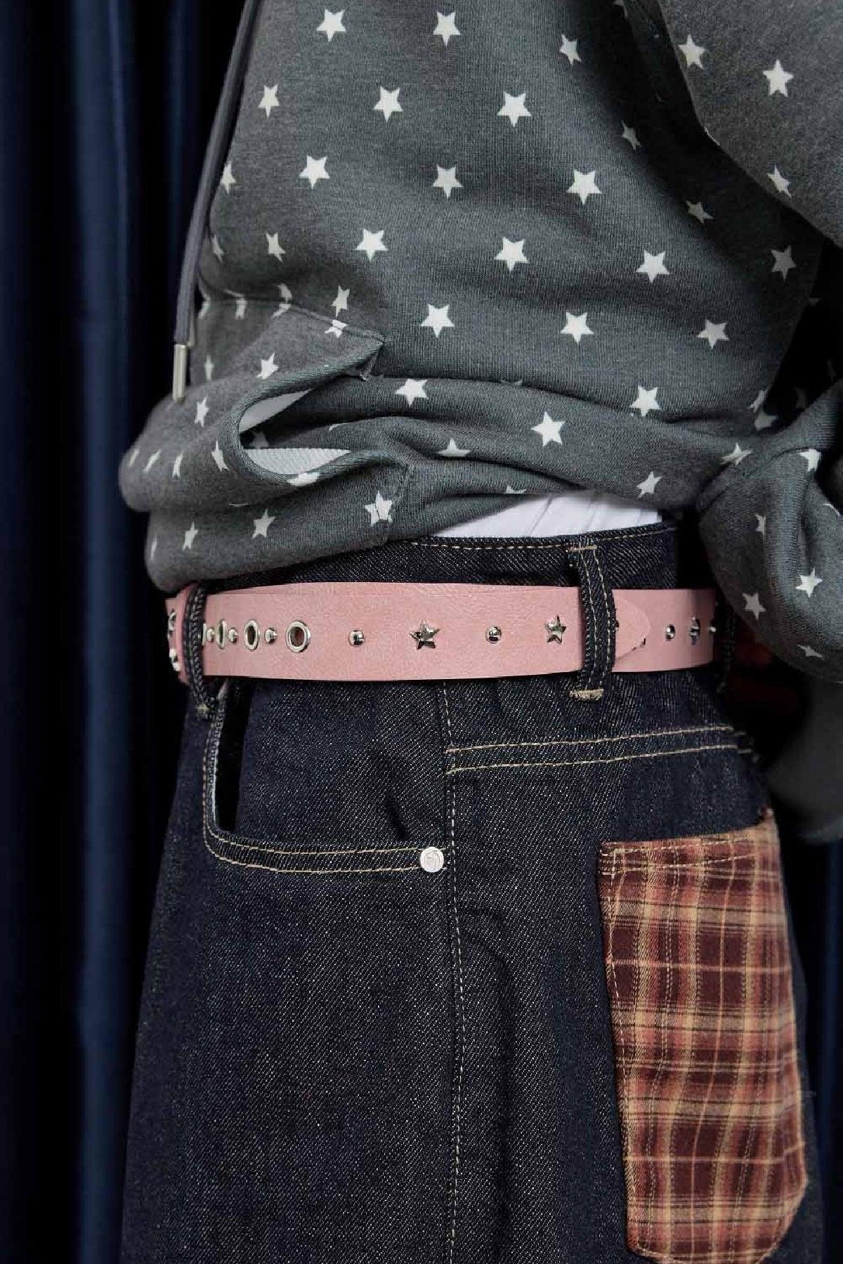Close-up of person wearing dark jeans with brown plaid pocket and a pink studded belt with star details, paired with a gray star-patterned sweatshirt