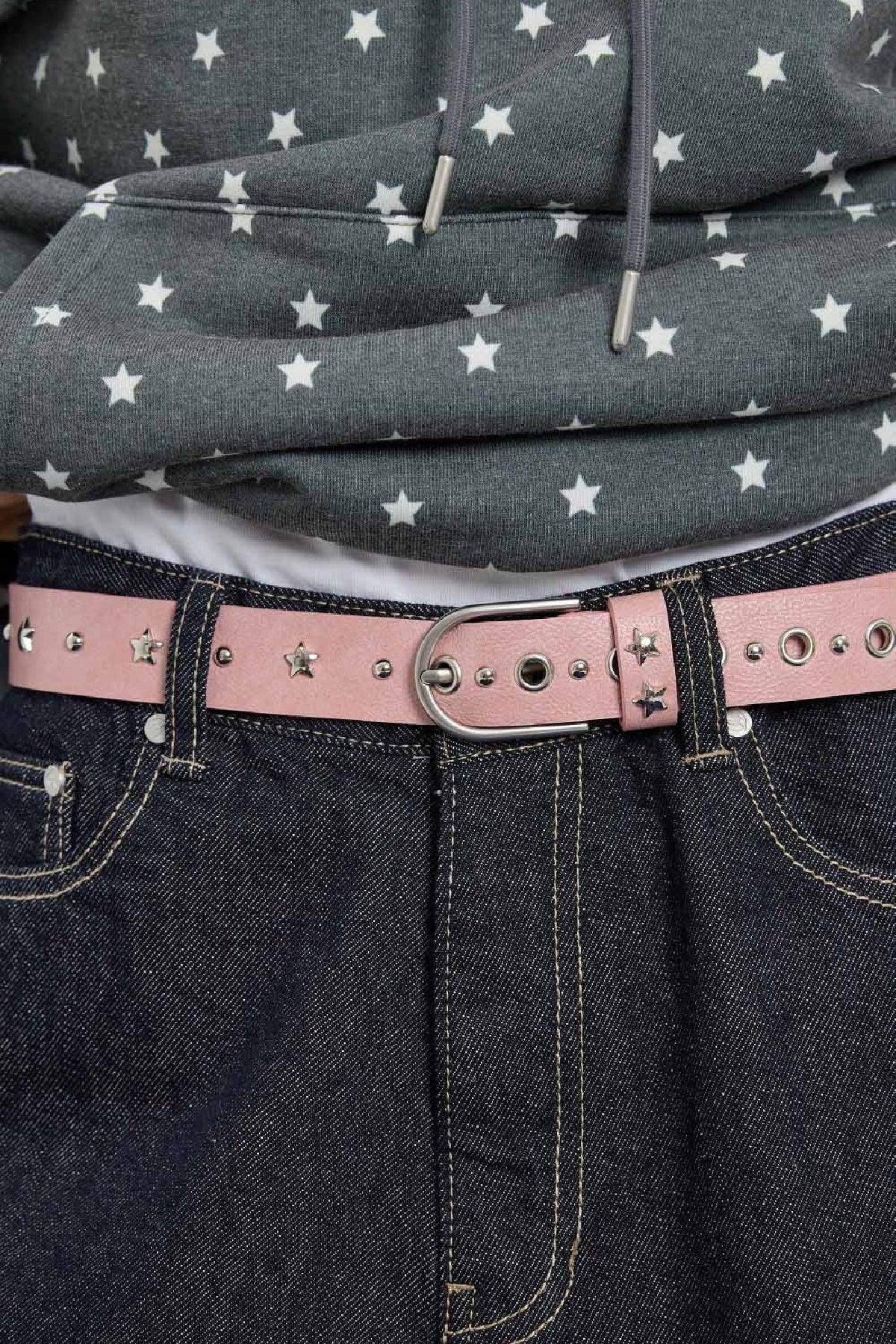 Close-up of pink studded leather belt with star accents on dark denim jeans and star-patterned gray hoodie
