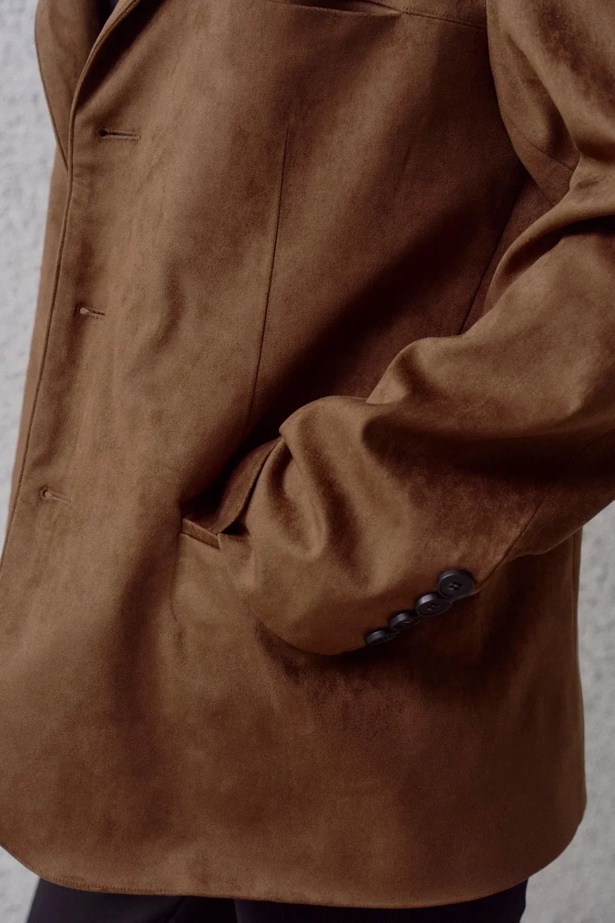 Close-up of brown suede blazer with black buttons and front pocket detail