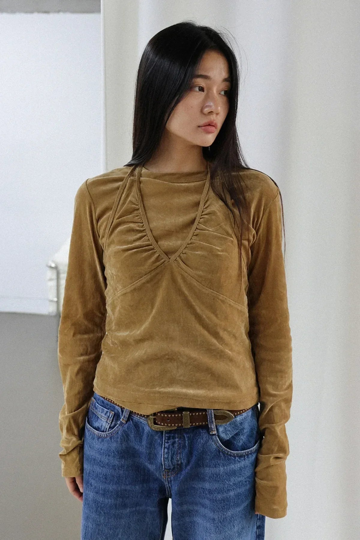 Woman wearing camel suede long-sleeve top paired with blue denim jeans and a brown belt