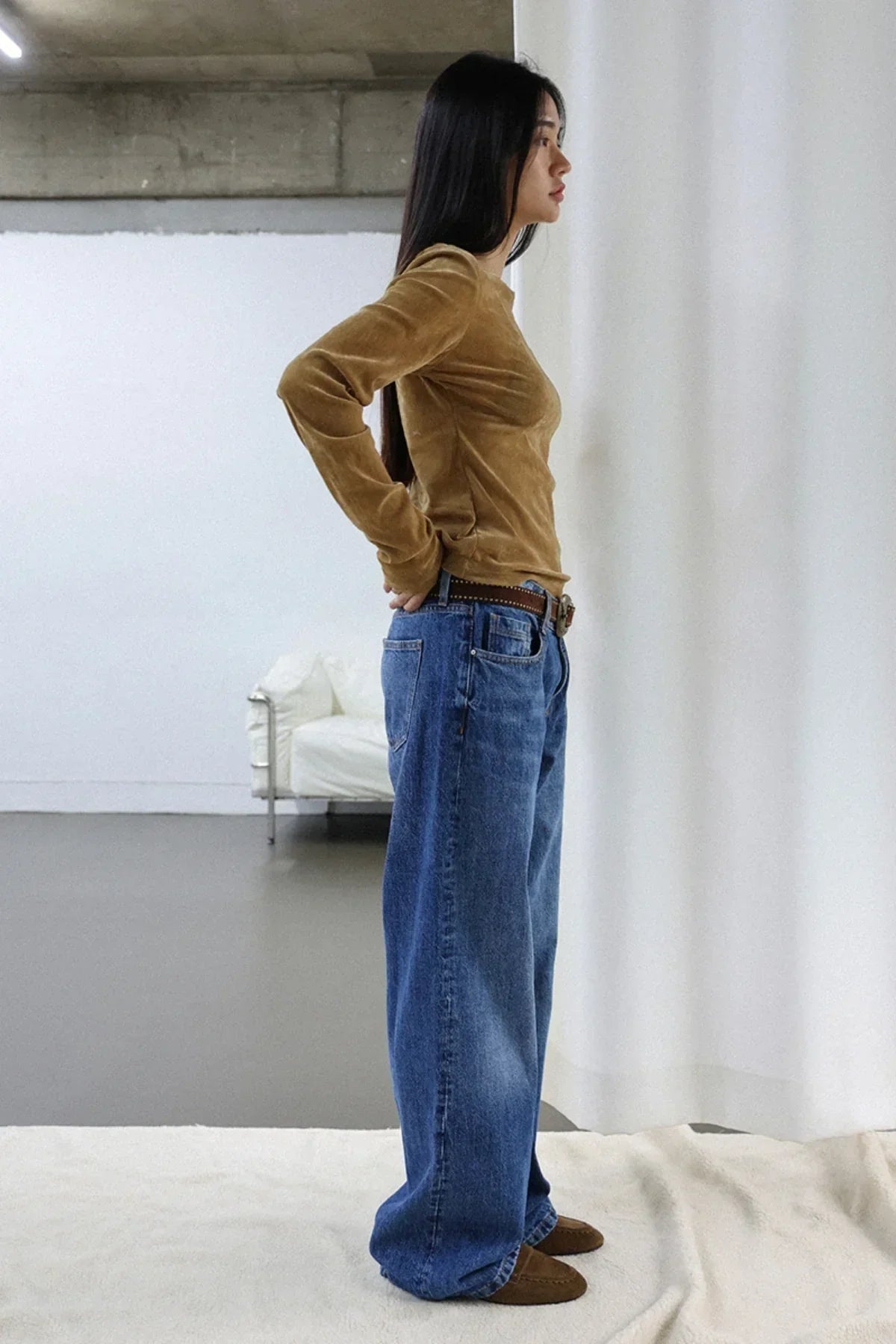Side view of woman wearing camel suede long sleeve top with loose blue jeans and brown shoes