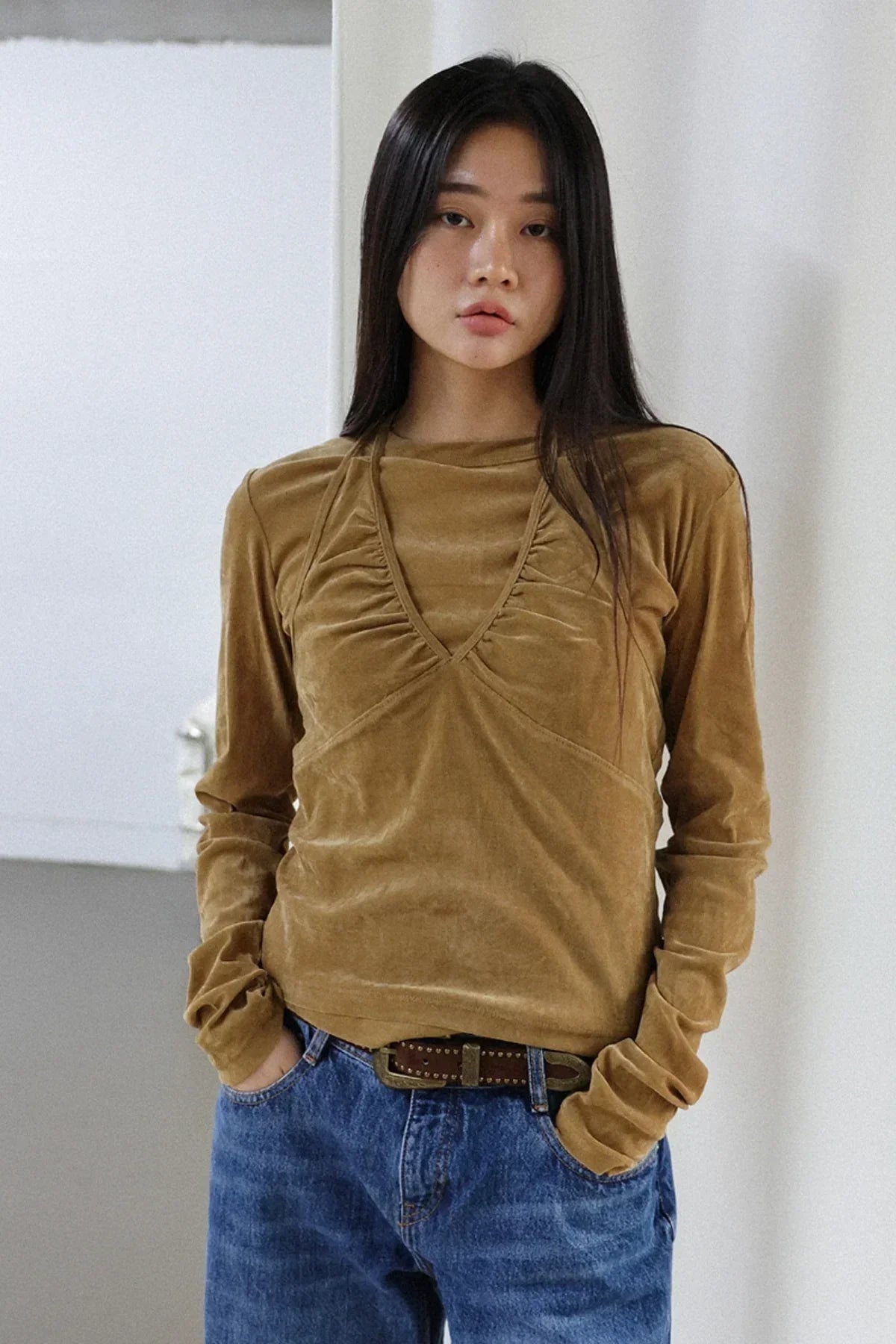 Young woman wearing camel suede long sleeve top and blue jeans in minimal indoor setting