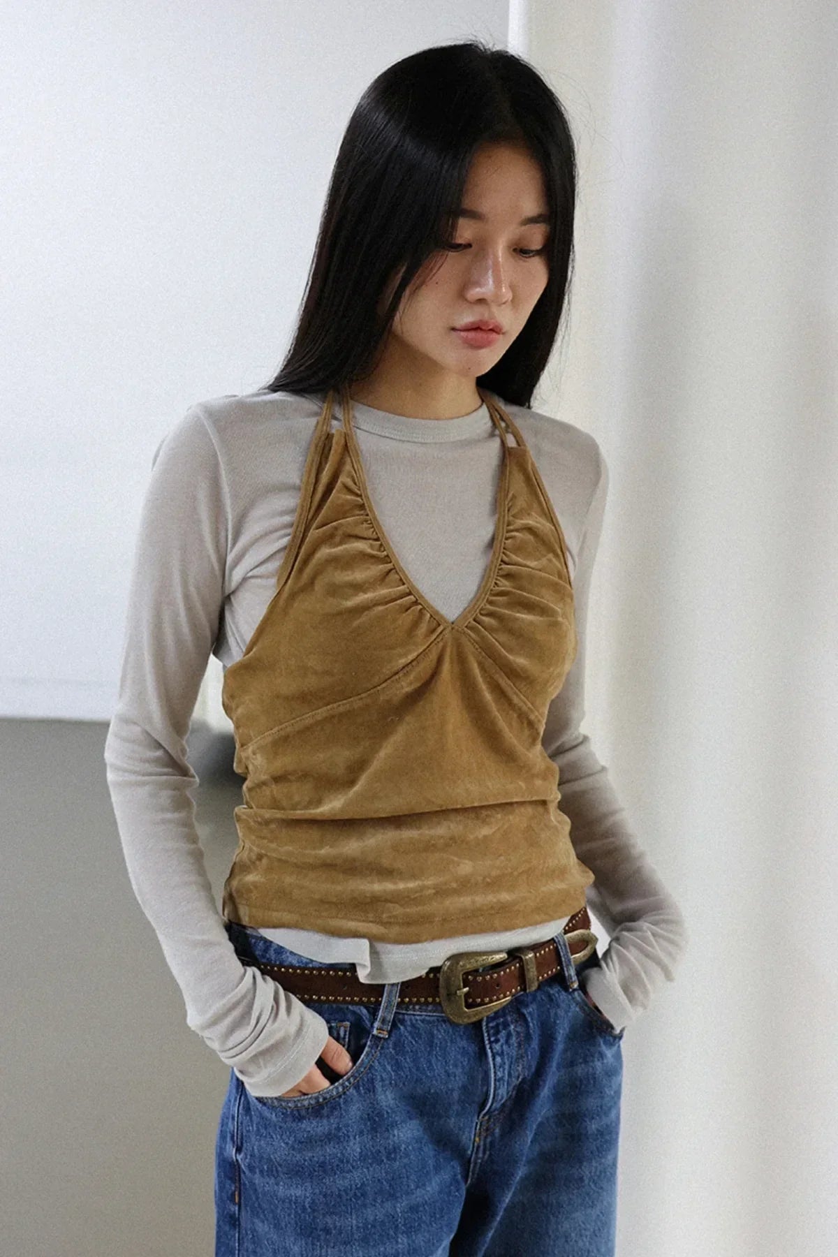 Woman wearing camel suede shirring bra top layered over gray long-sleeve shirt with blue jeans and belt