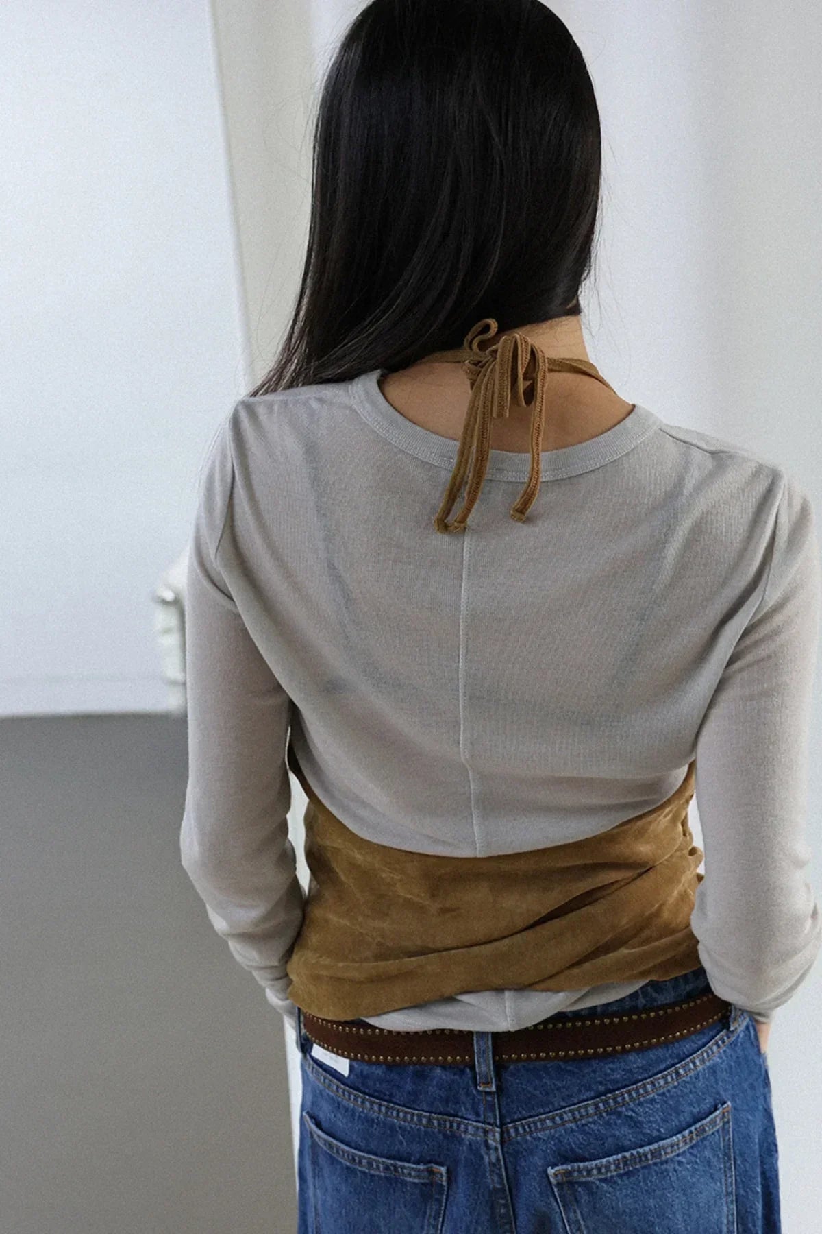 Back view of a woman wearing a camel suede shirring bra top over a long sleeve beige shirt with blue jeans