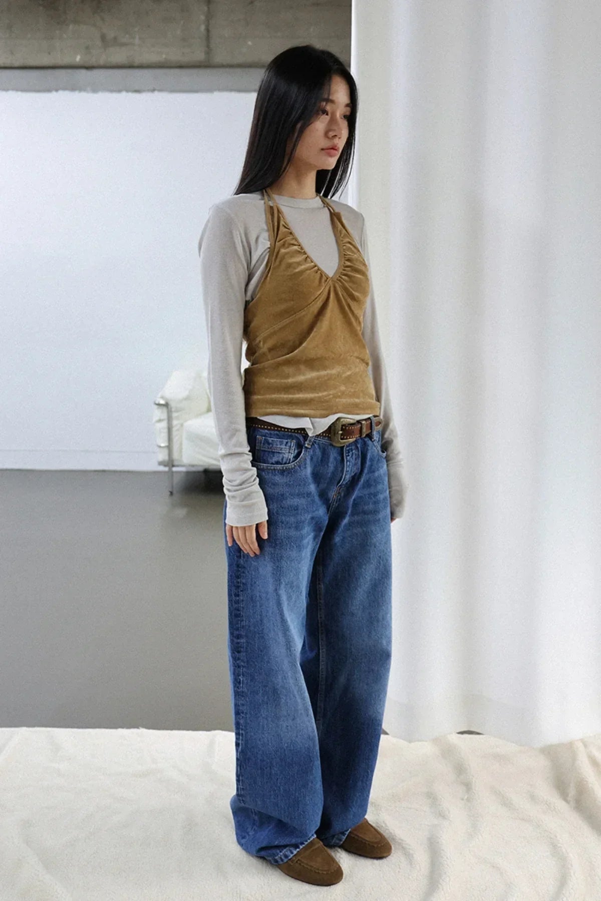 Woman wearing camel suede shirring bra top layered over long sleeve shirt with wide-leg jeans in minimalist indoor setting