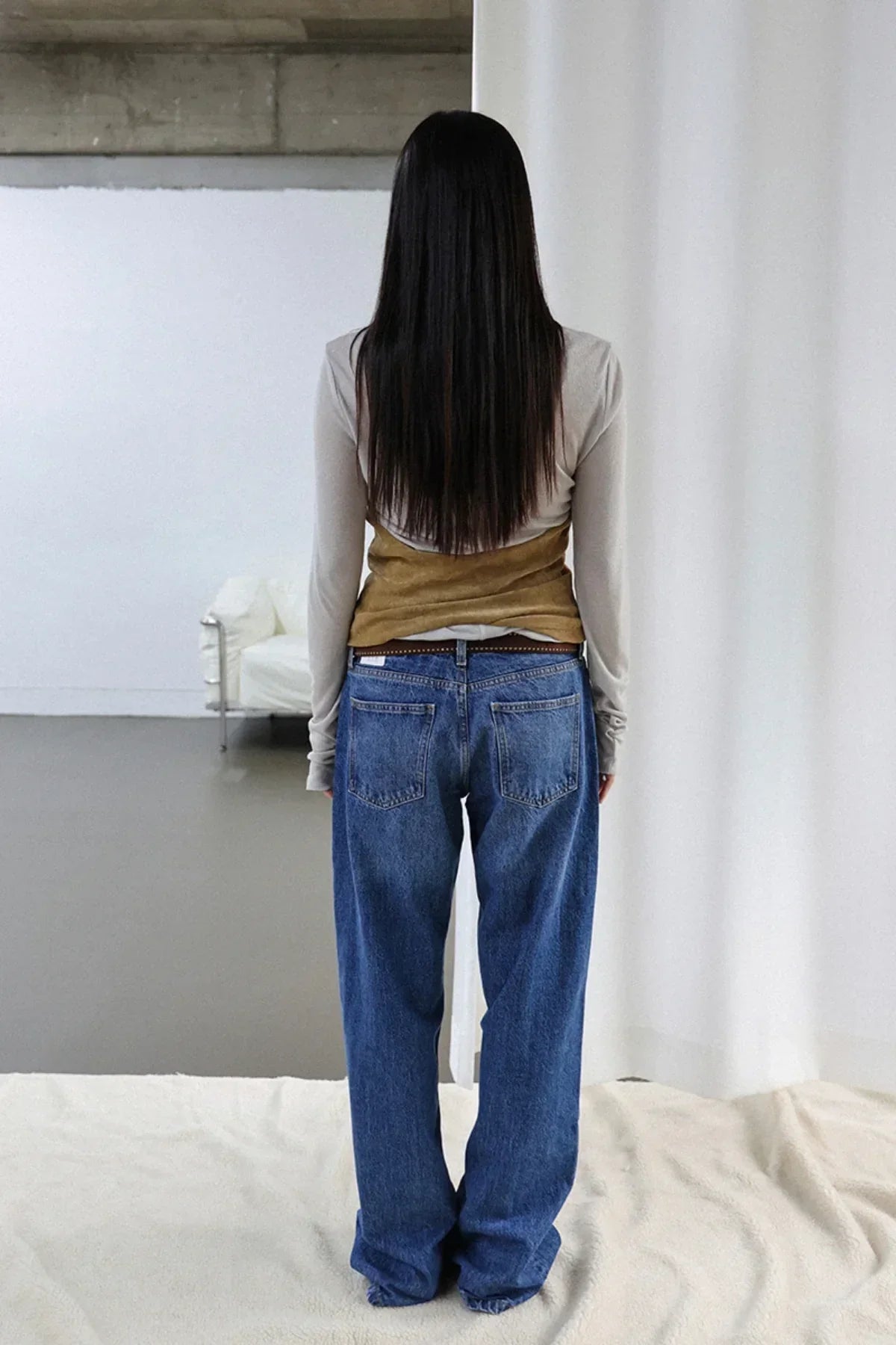 Model wearing camel suede shirring bra top over beige long sleeve shirt and loose blue jeans, standing indoors
