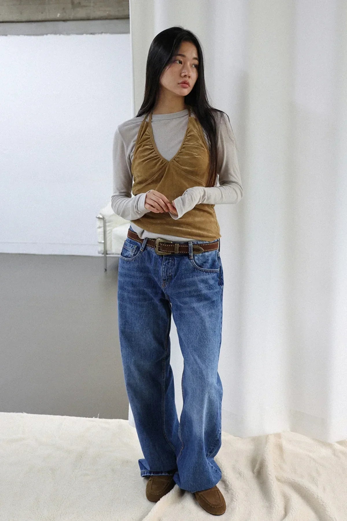 woman wearing camel suede shirring bra top over long sleeve shirt with blue jeans and brown moccasin shoes in studio