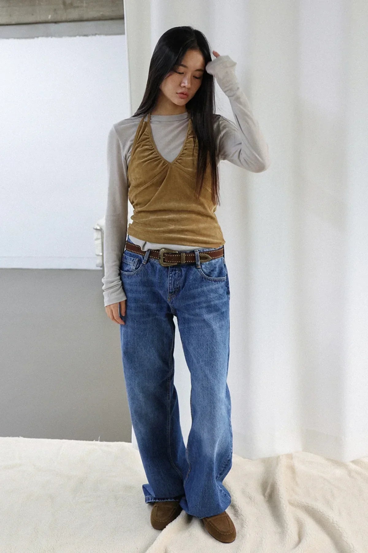 Young woman wearing camel suede shirring bra top over long sleeve gray shirt with blue jeans and brown shoes