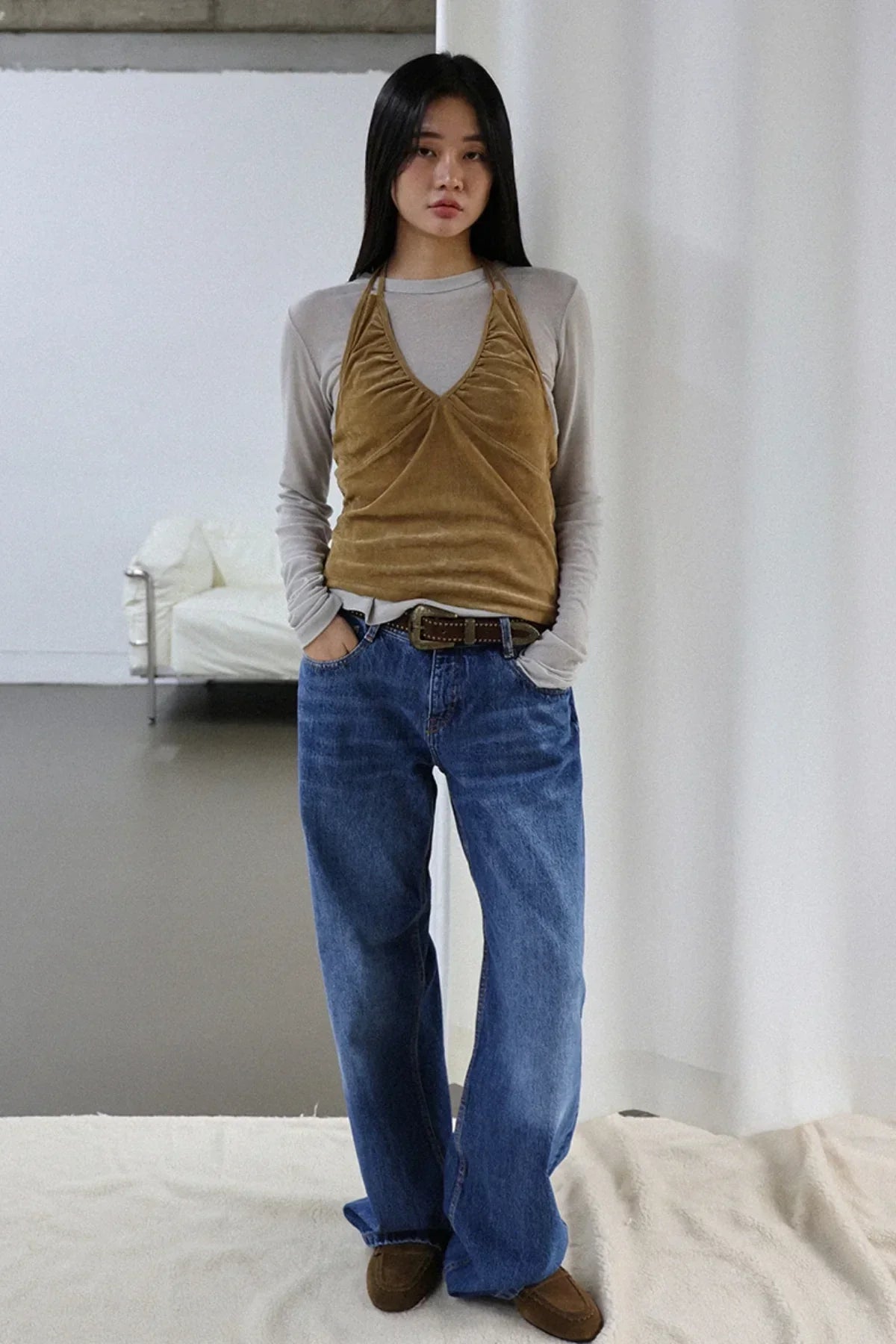 Woman wearing camel suede shirring bra top over long-sleeve gray shirt with blue jeans in minimalist studio