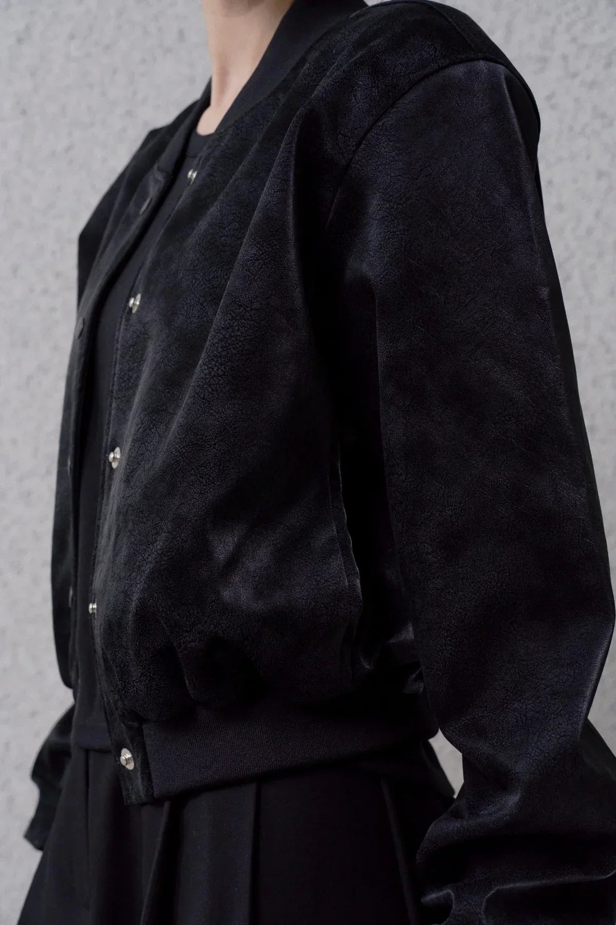 Close-up of a black suede stadium jacket with snap buttons and ribbed hem, worn over black clothing