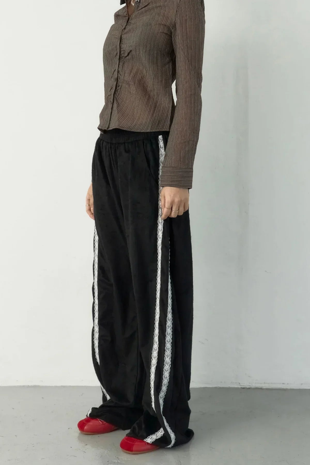 Close-up of person wearing black suede pants with white lace side stripes and red shoes