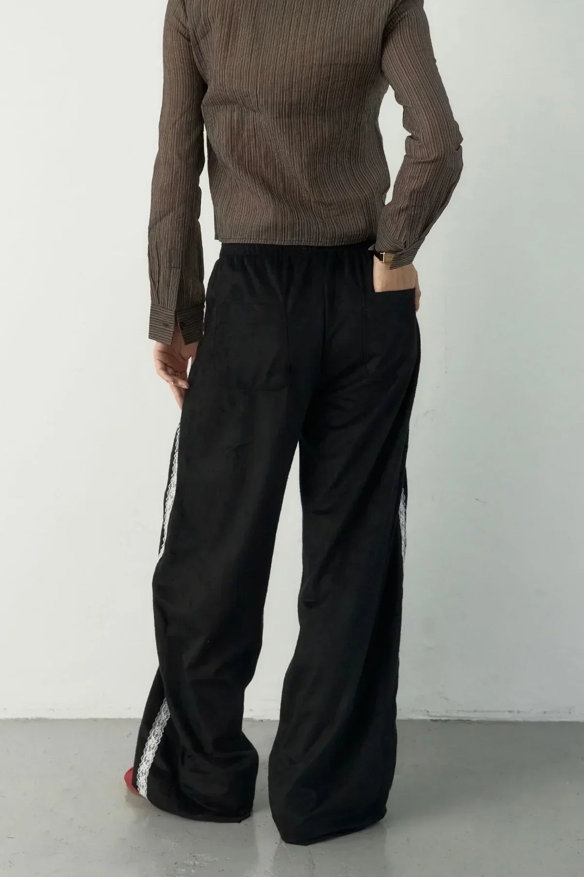 Person wearing black wide-leg suede pants with white lace side tape, brown ribbed long-sleeve top, standing on gray floor