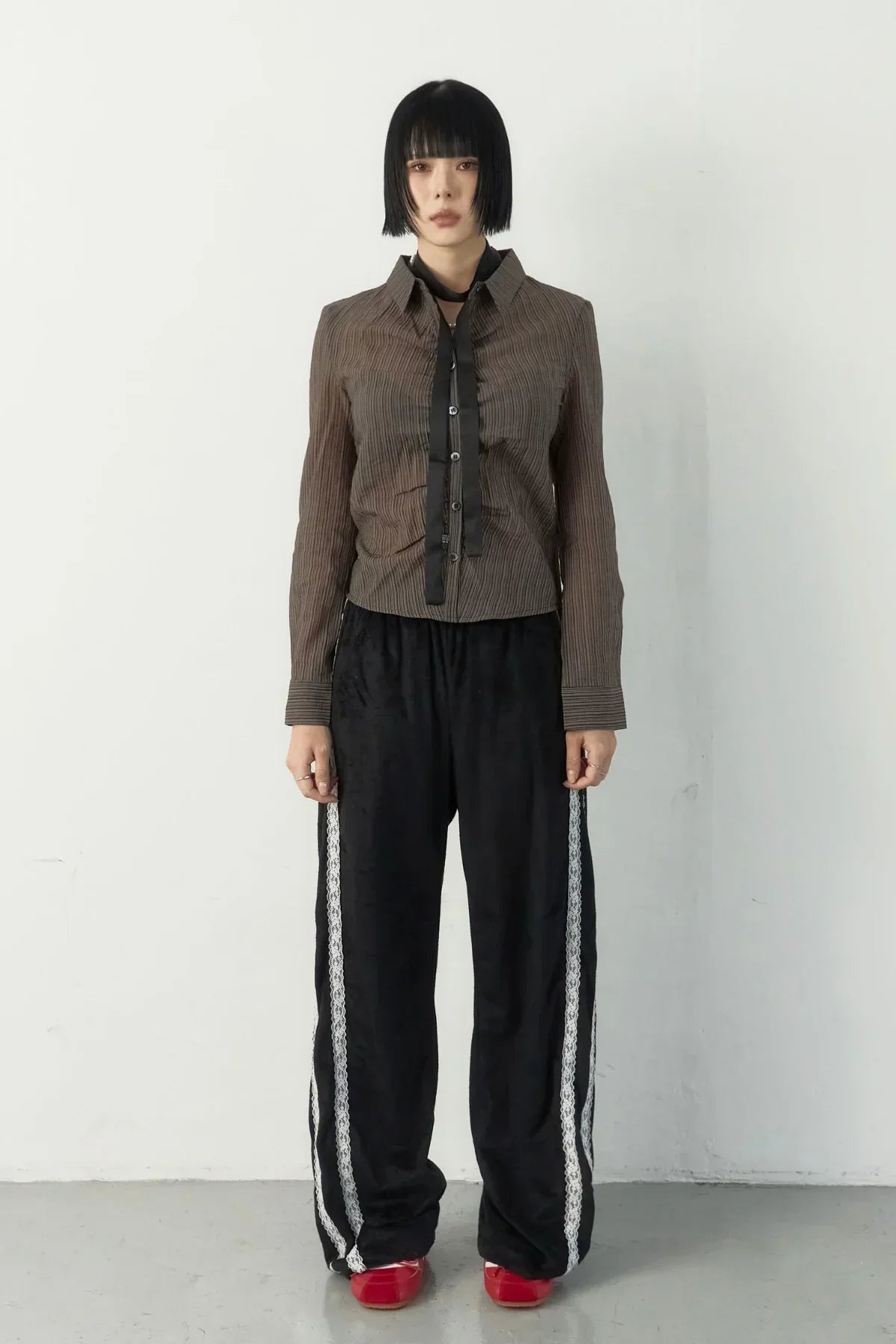 Model wearing black suede pants with white side lace stripes, brown striped shirt, and red shoes