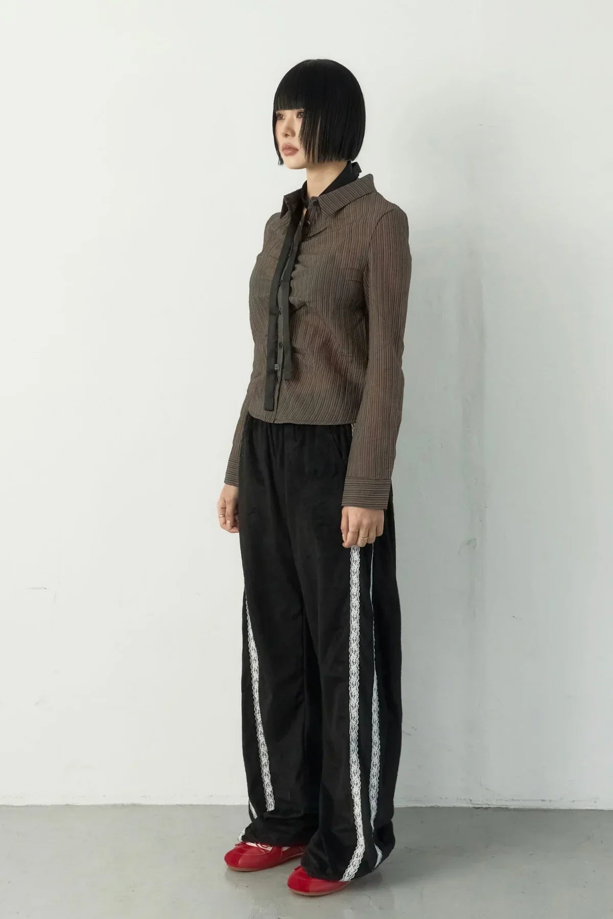 Model in brown striped shirt, black wide suede pants with white side lace tape, and red shoes