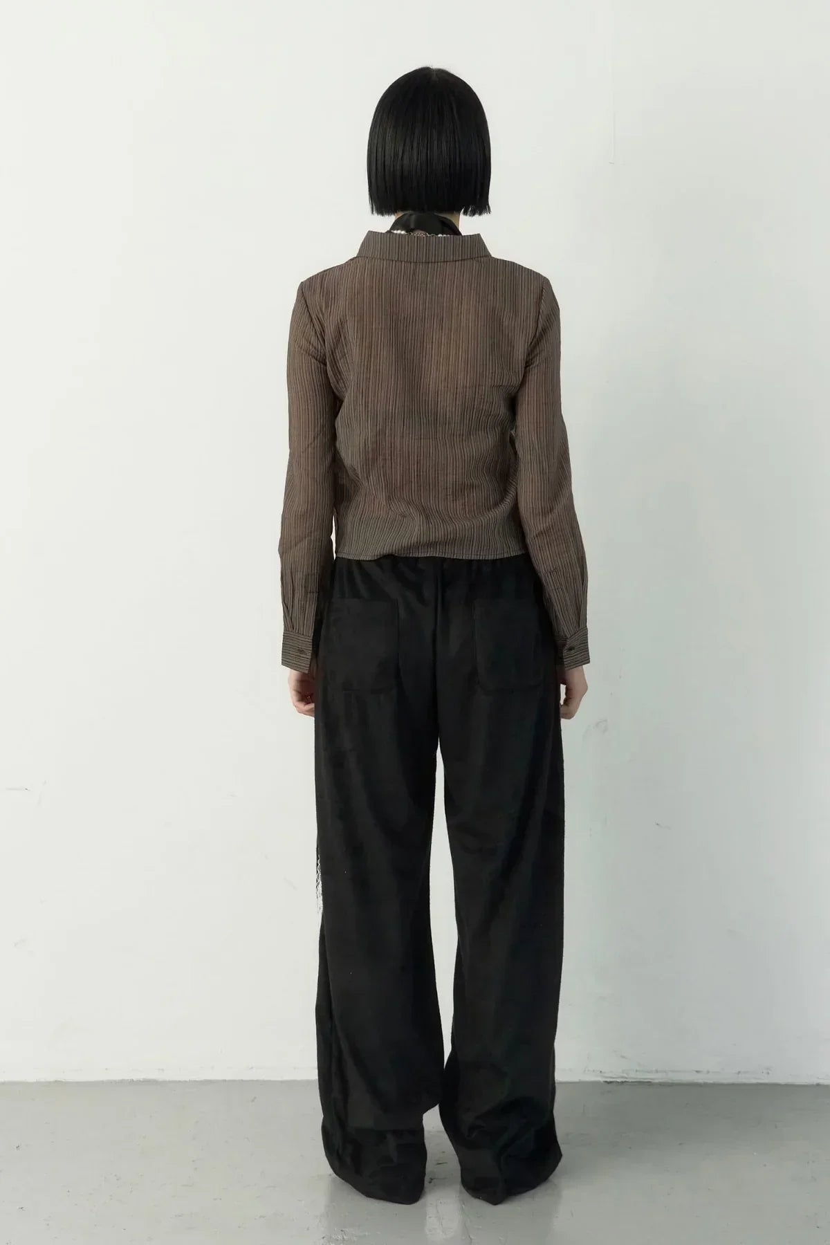 Back view of a model with black bob haircut wearing brown striped top and loose black suede pants
