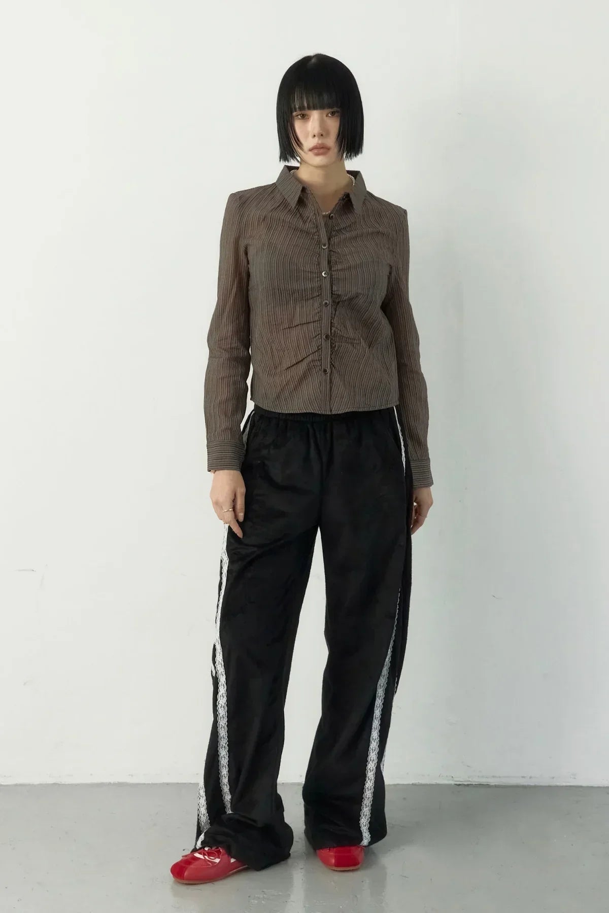 Model wearing brown ruched blouse and black wide-leg pants with white lace tape in studio
