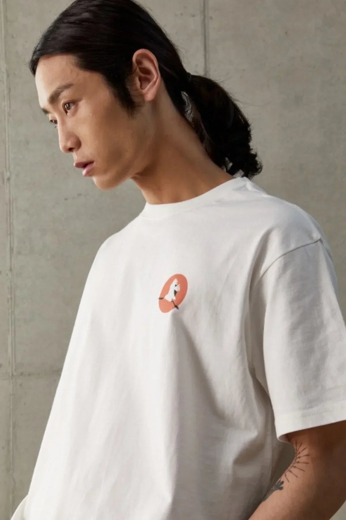 Young man in white t-shirt with orange sun and bird graphic, concrete wall background