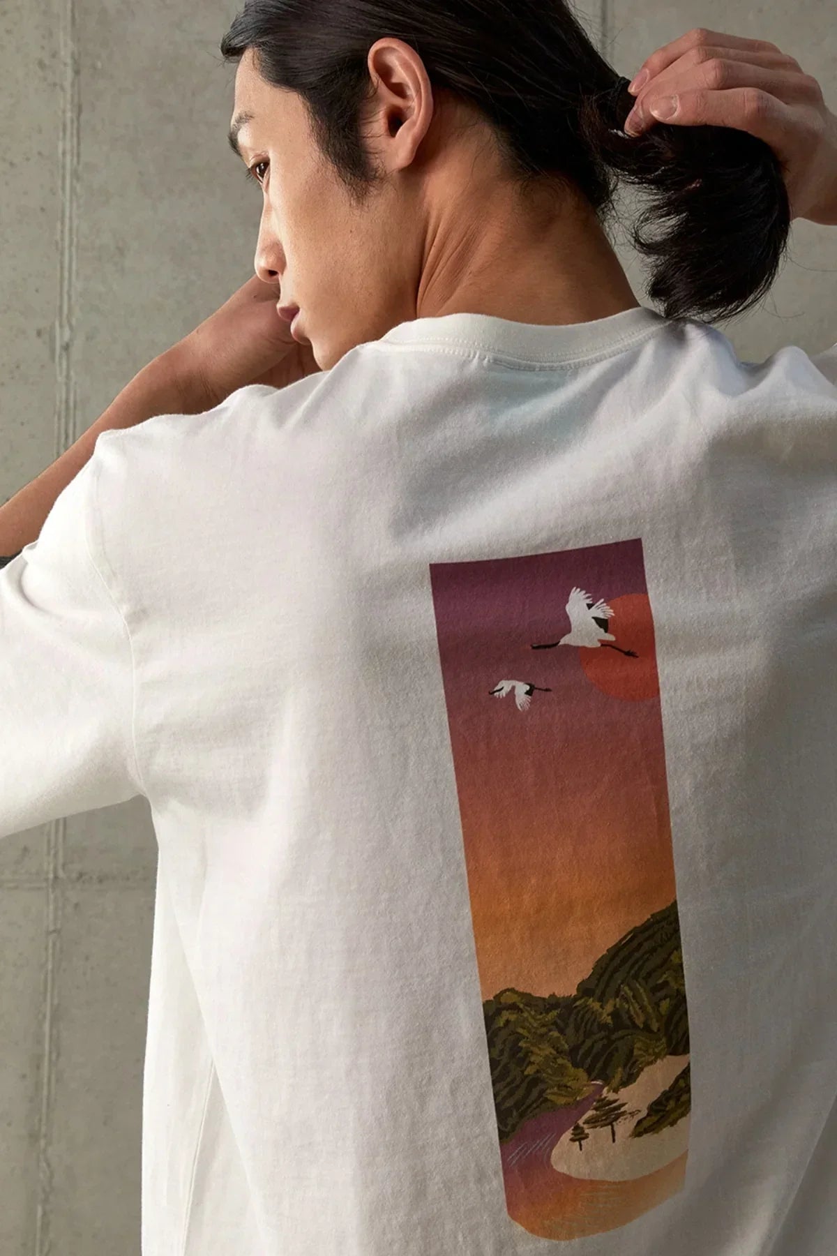 White t-shirt with a sunset graphic featuring flying cranes and a mountainous landscape