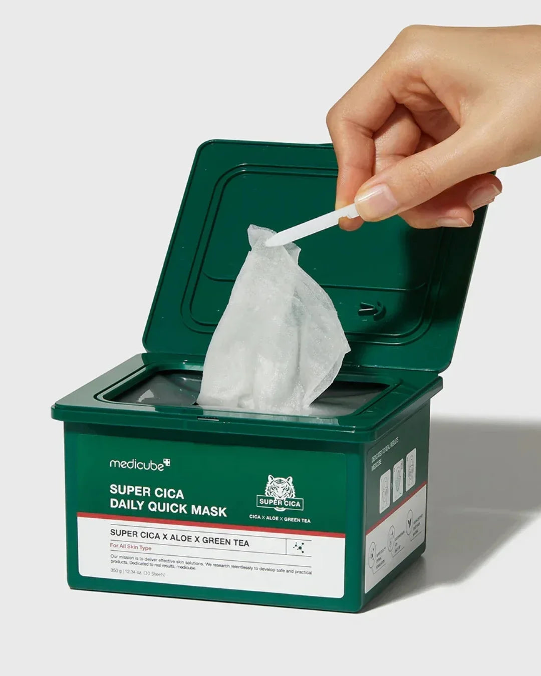 Hand pulling a wet skincare sheet mask from green Medicube Super Cica Daily Quick Mask container