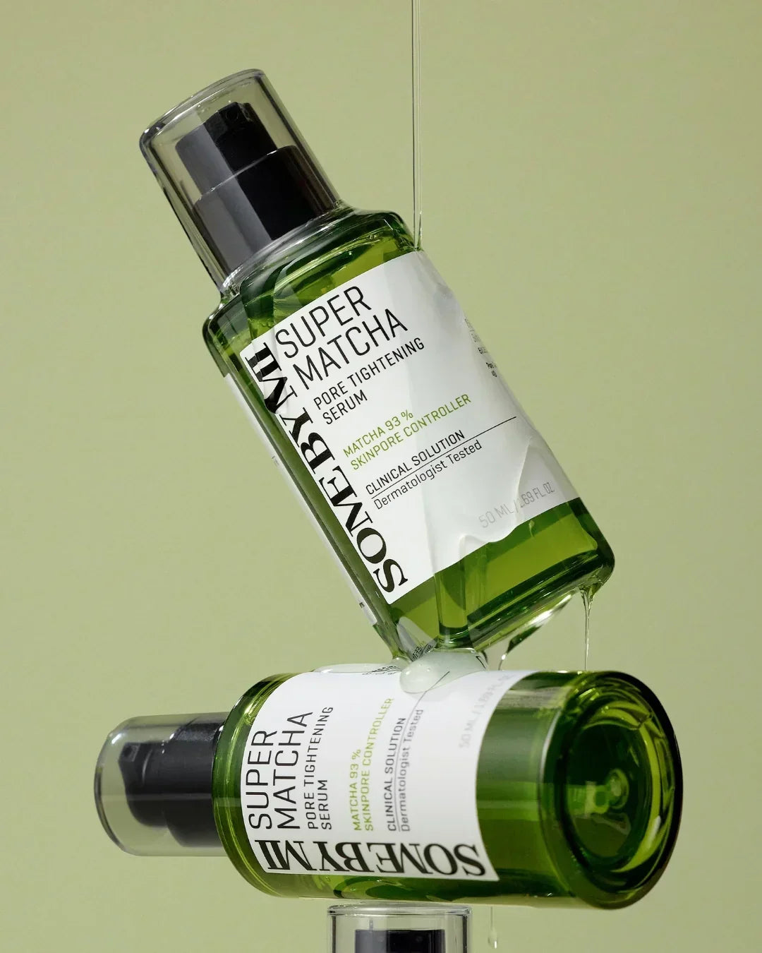 Two green bottles of Some By Mi Super Matcha Pore Tightening Serum with clear liquid drip on a light green background